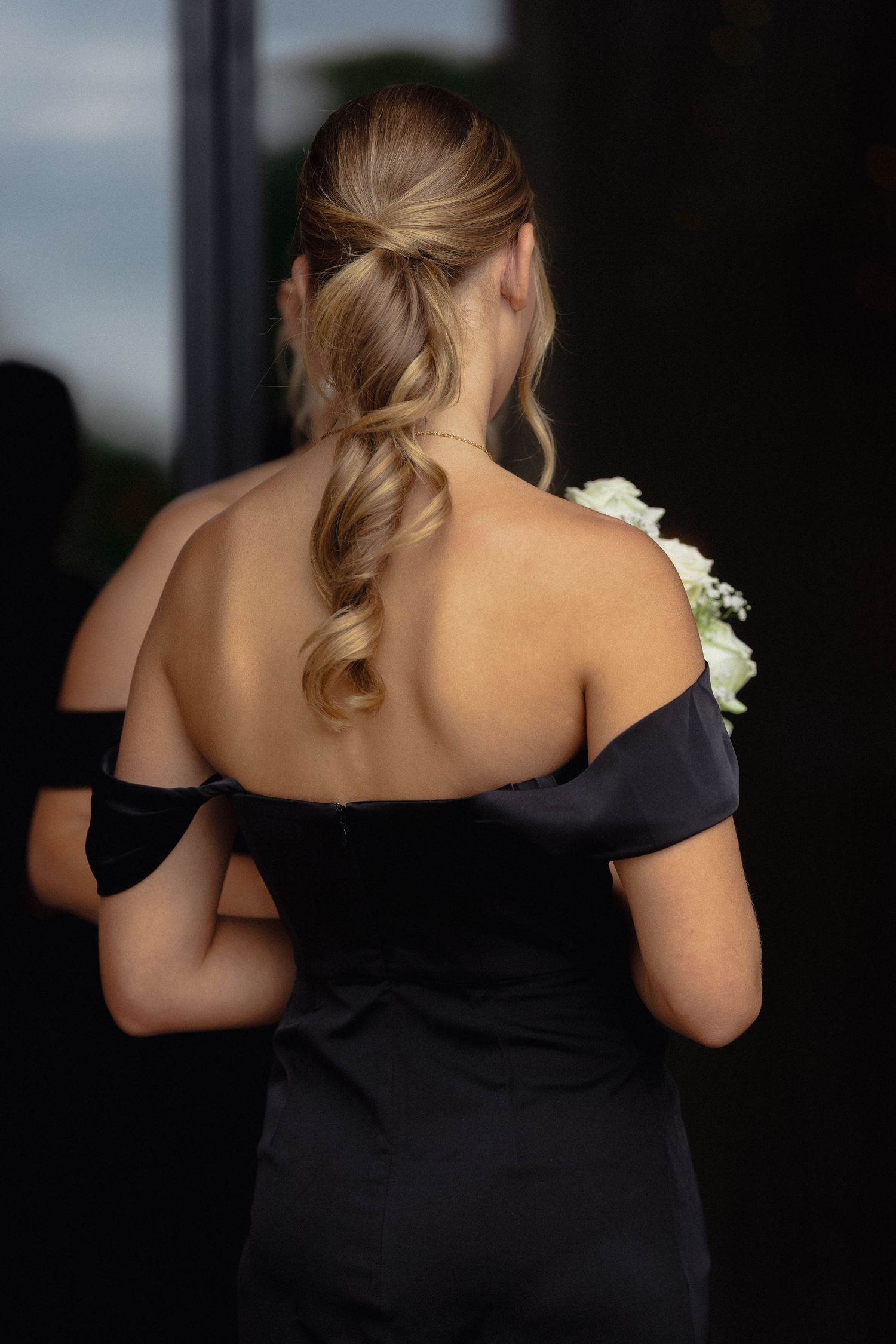 Bridesmaids in elegant black off-shoulder dresses stand together at a wedding venue.