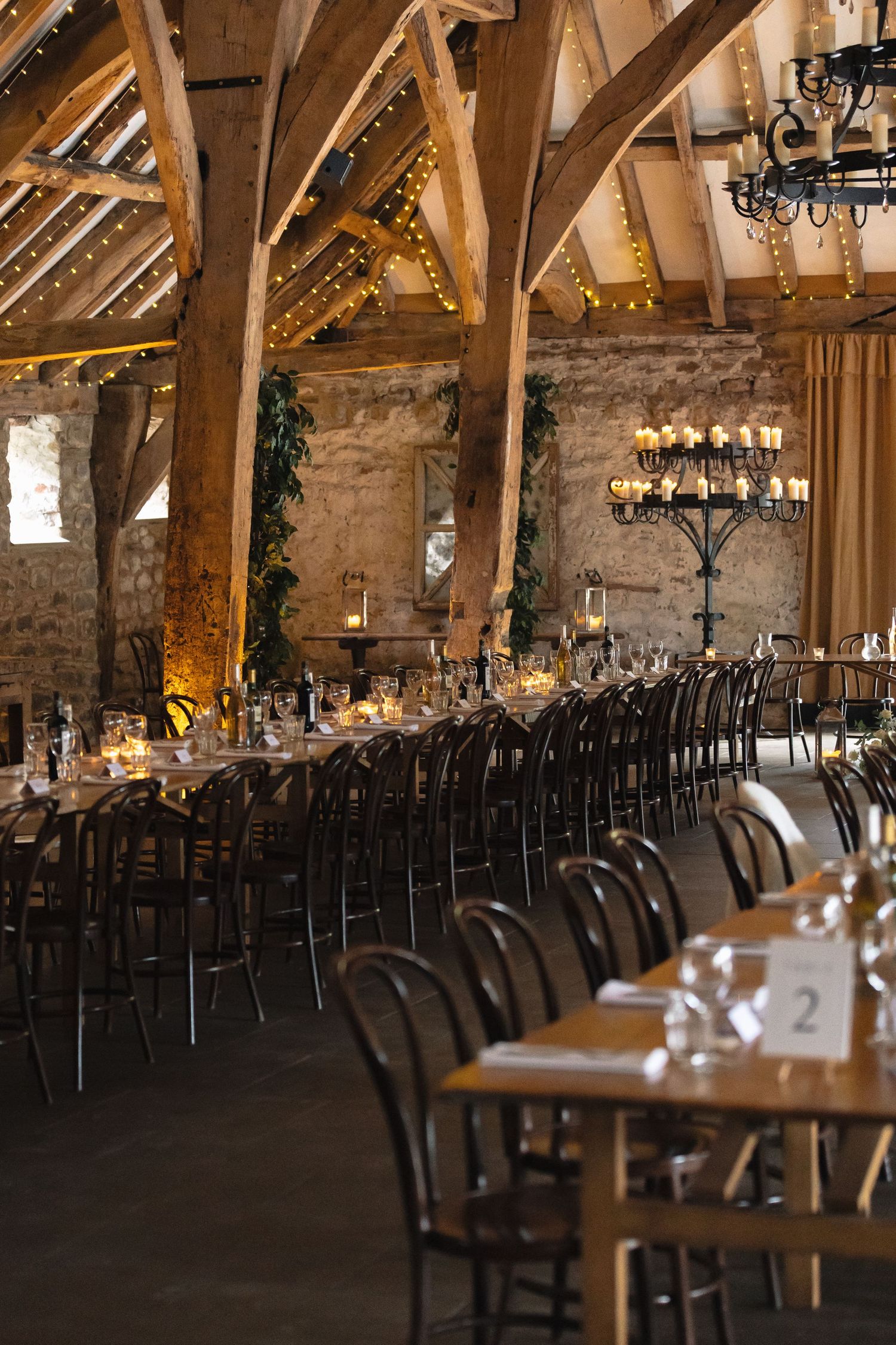 Rustic barn wedding venue with wooden beams, chandeliers and long tables set for dinner reception.