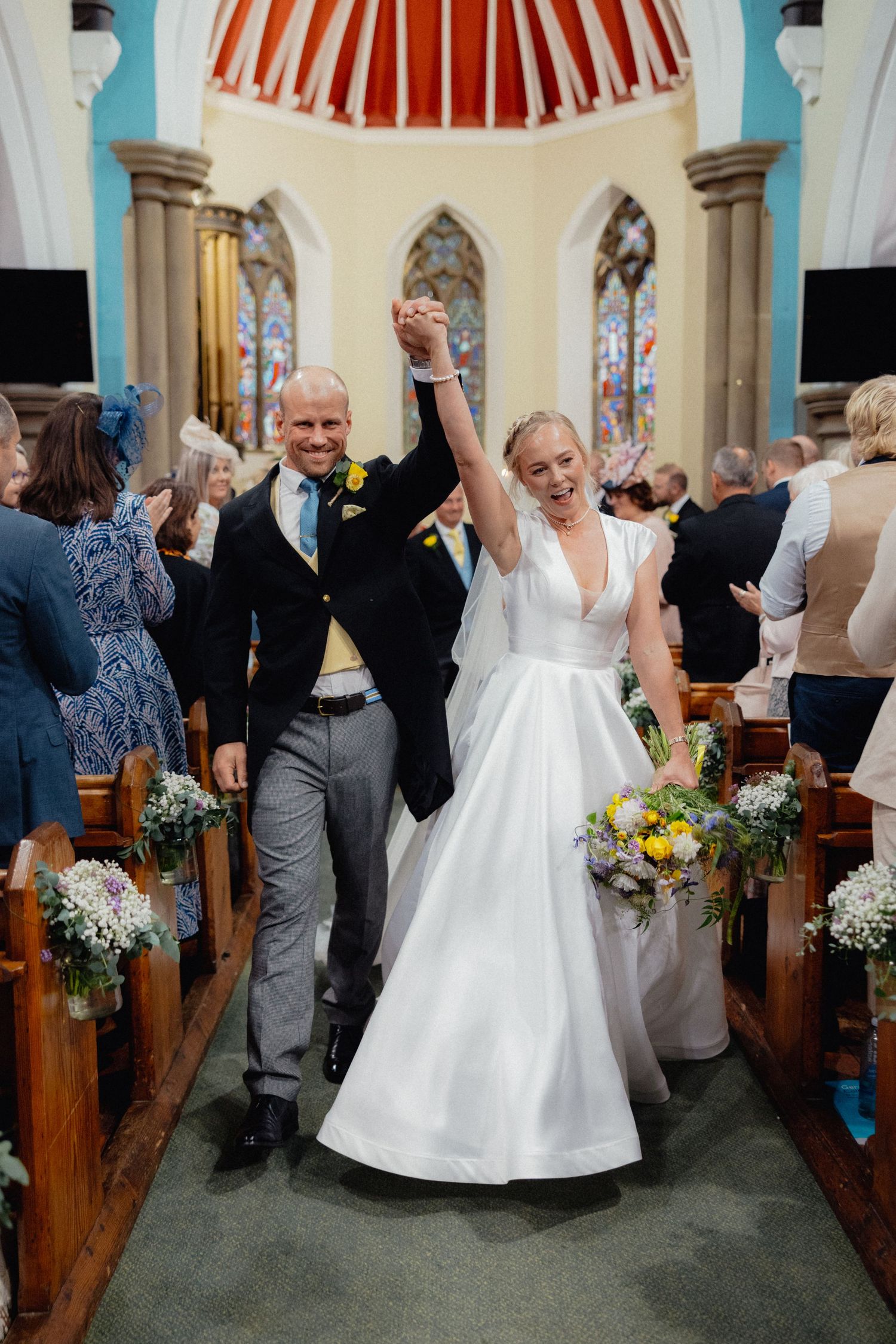 Jubilant newlyweds celebrate while walking down church aisle after ceremony.