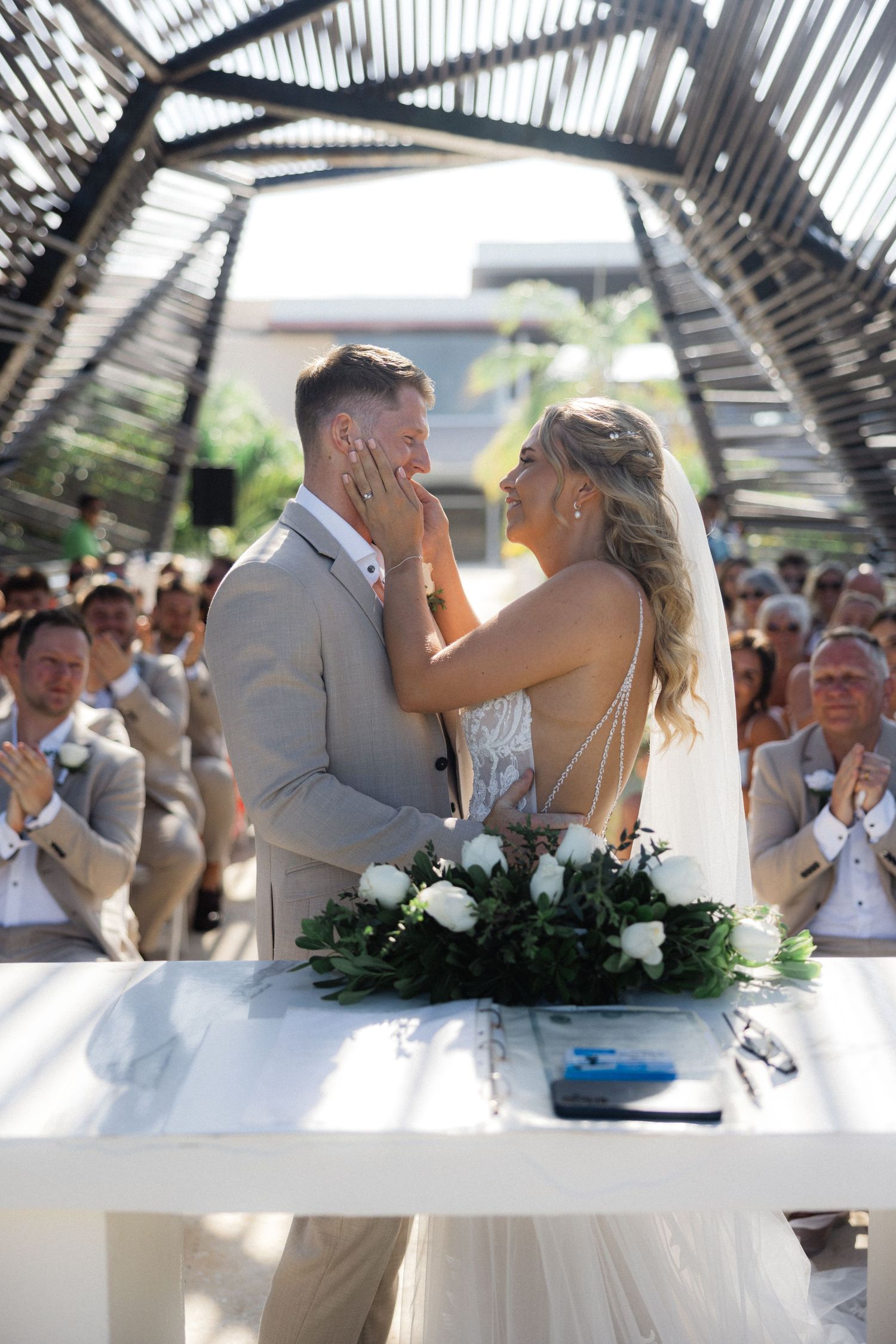 Wedding couple embraces during emotional moment as guests celebrate in background.