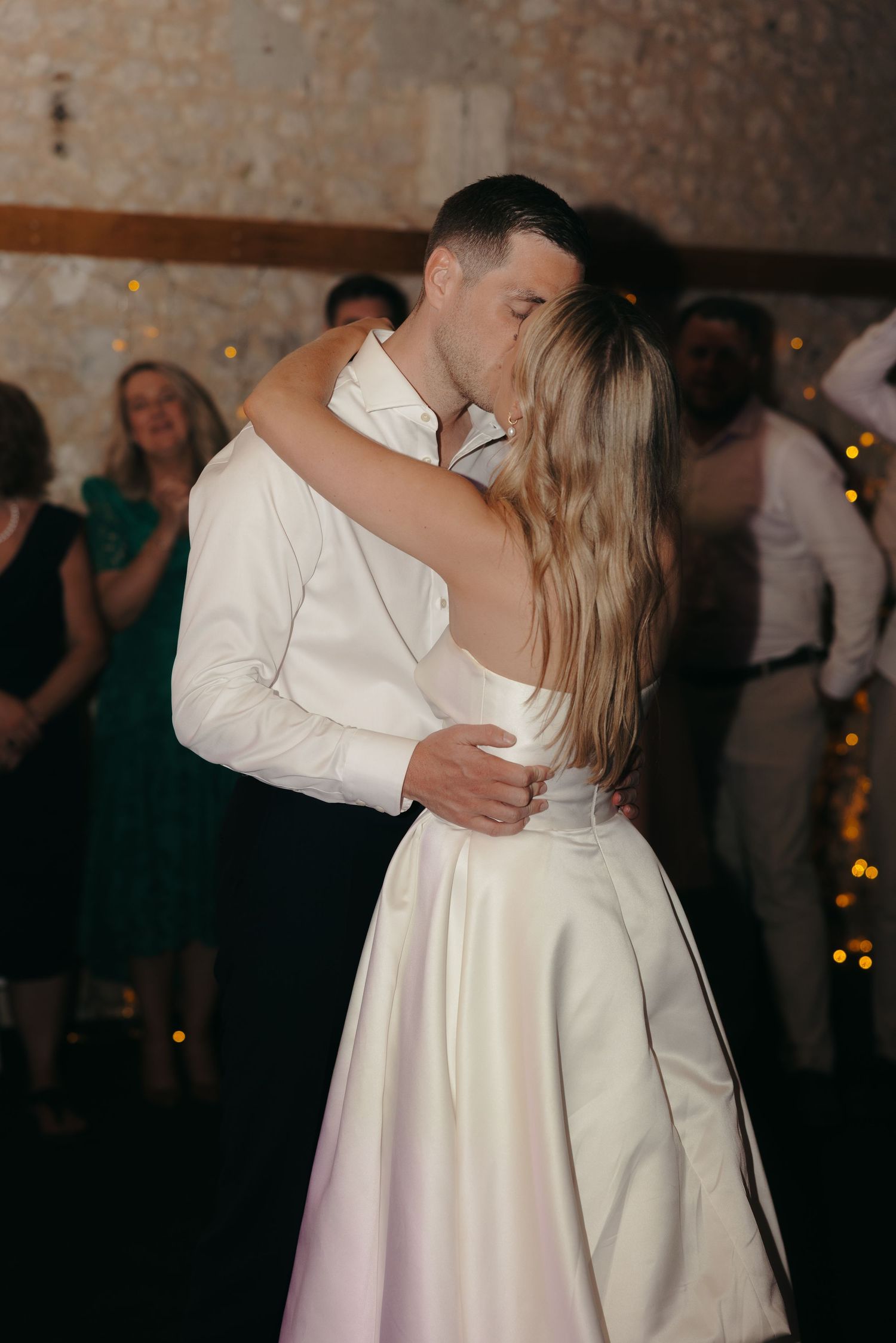Couple sharing a romantic dance in an elegant stone-walled venue with string lights.