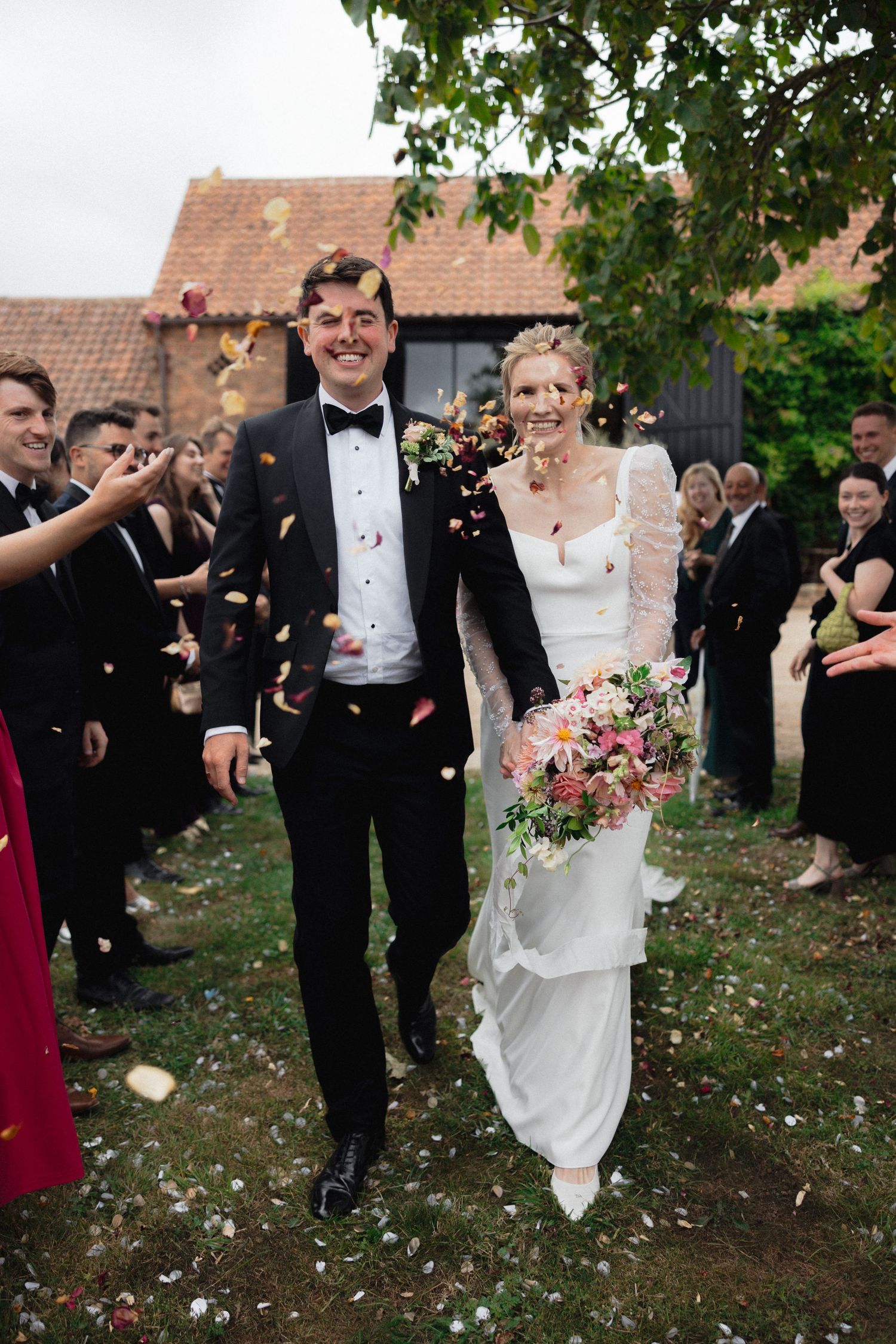 Wedding couple and guests celebrate with confetti toss in outdoor garden setting.