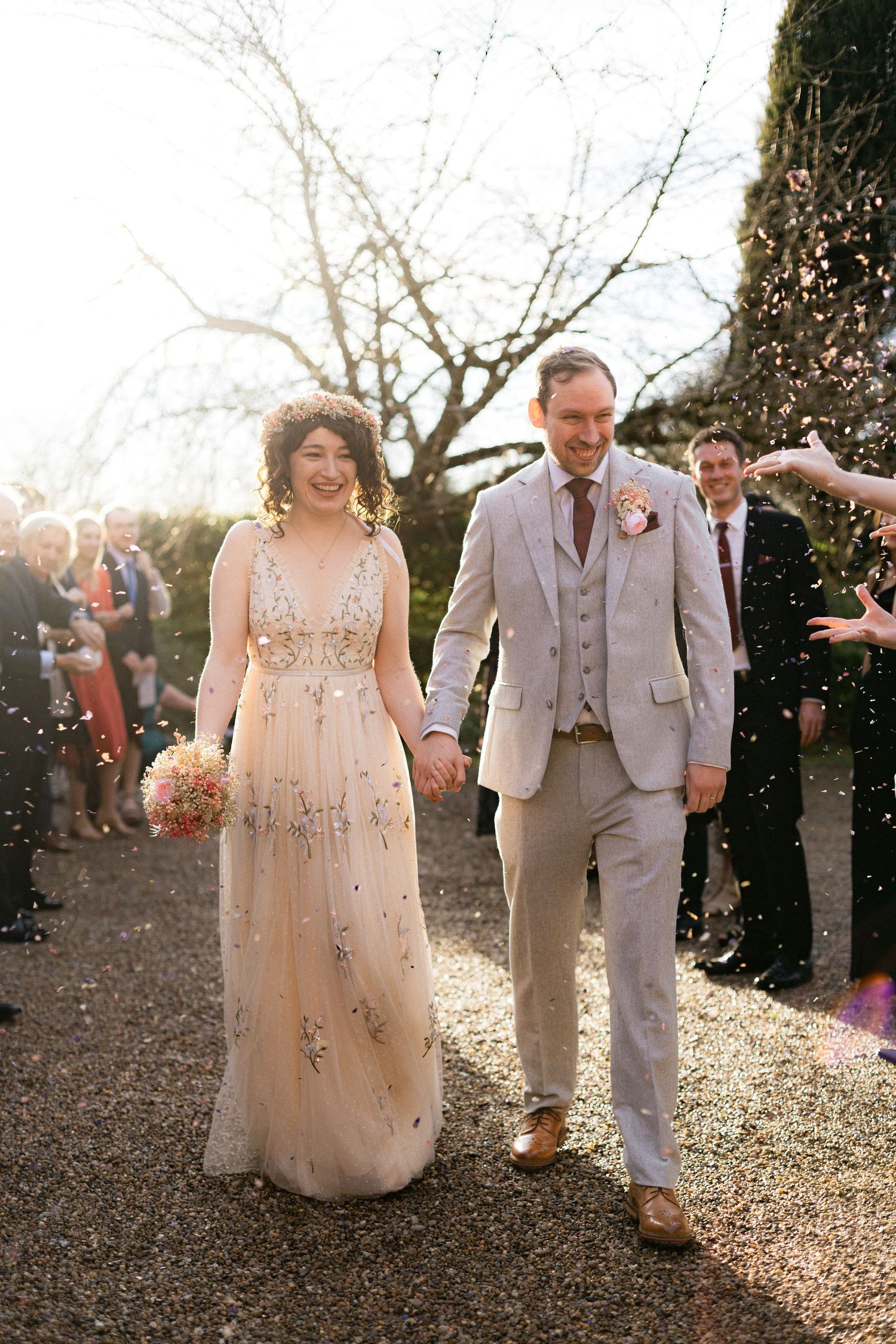 Newlyweds walking hand in hand while guests throw confetti in golden sunset light.