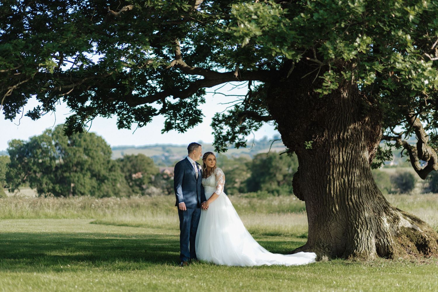 A romantic wedding photoshoot under a majestic oak tree in a rural field.