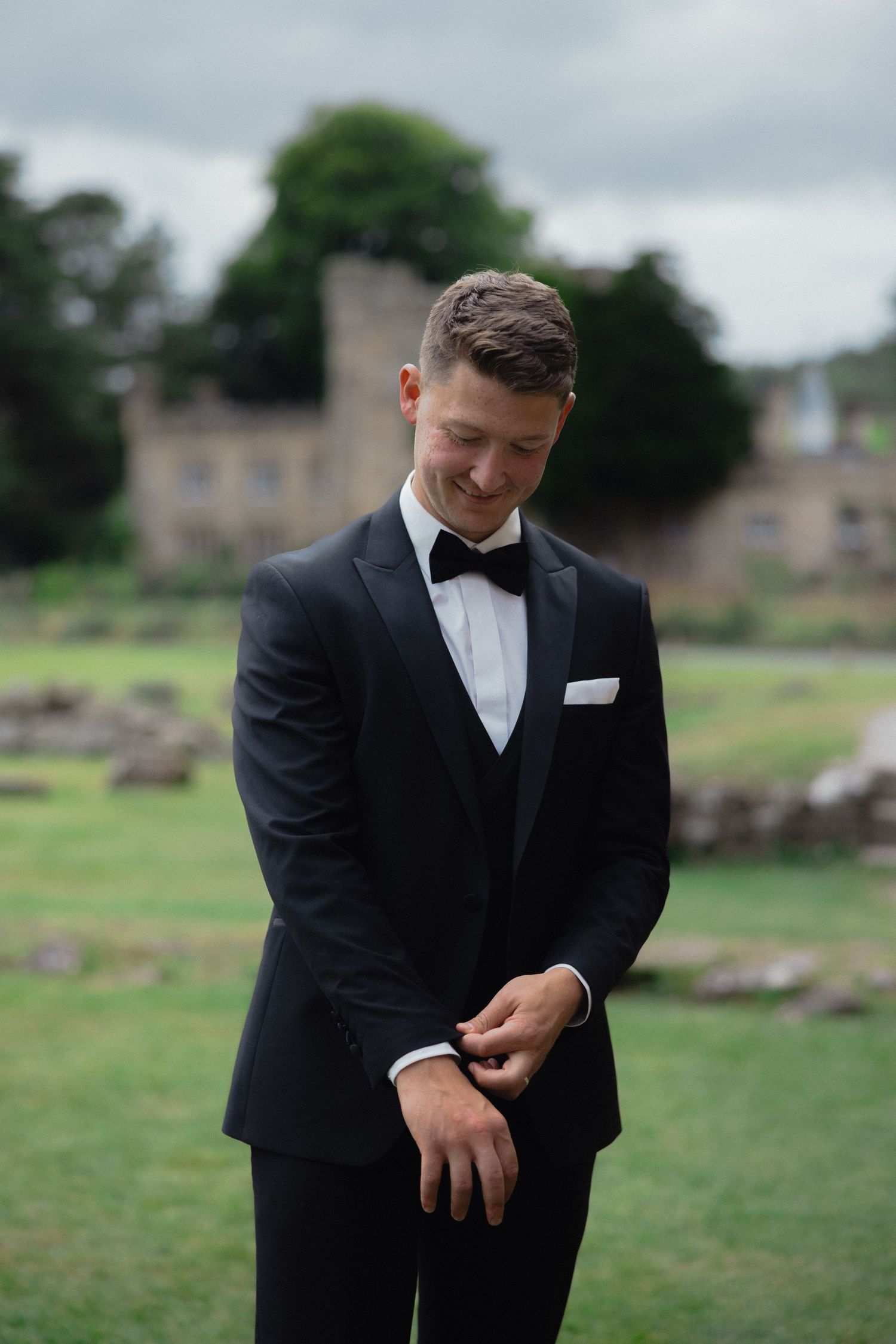 Groom in classic black tuxedo adjusts his attire during outdoor wedding shoot.