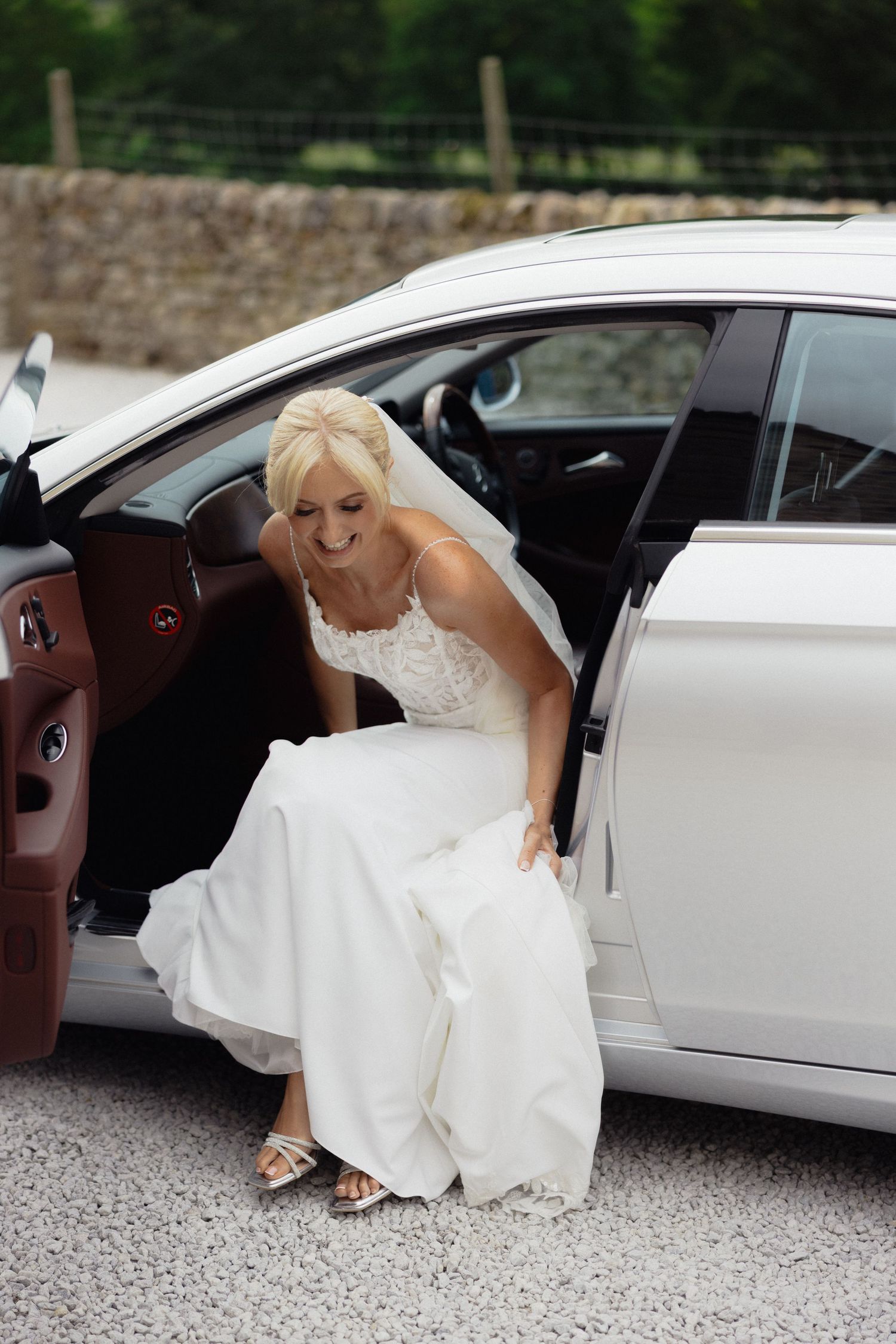 A bride in a white wedding dress carefully steps out of a white car.