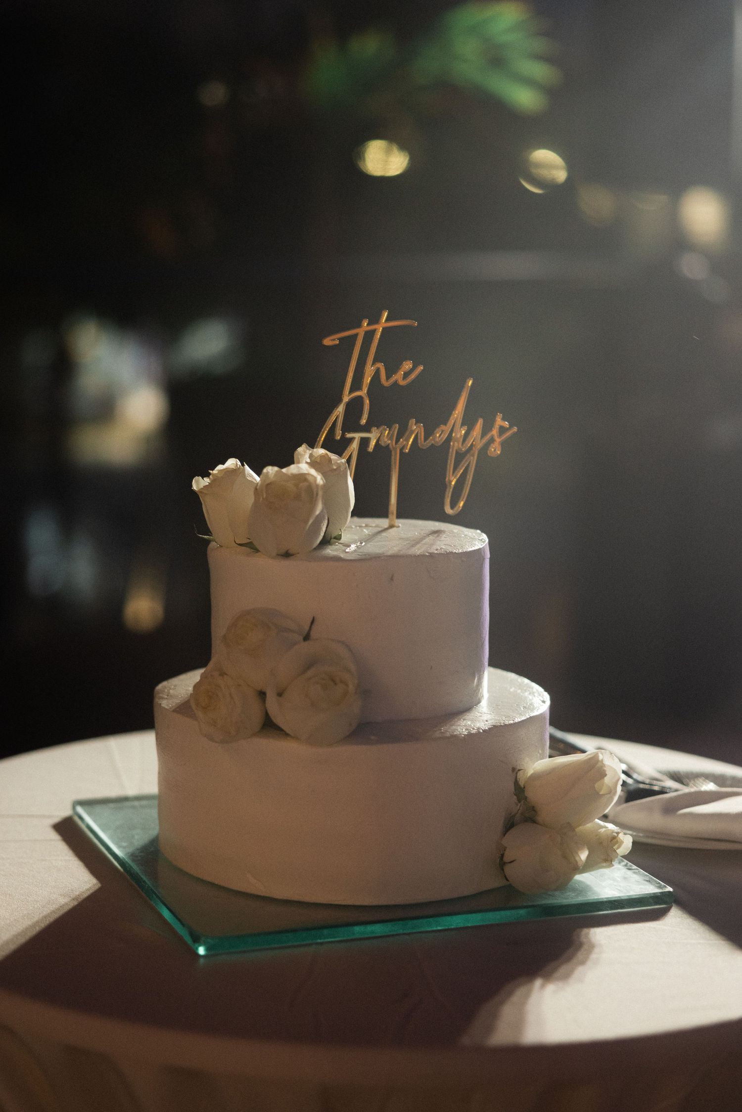 White wedding cake with elegant script topper displayed on glass stand.