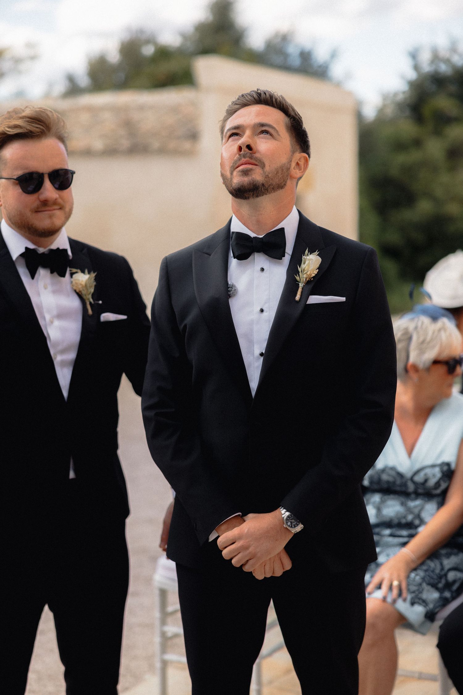 Groomsmen in classic black tuxedos and bow ties share a moment during the wedding ceremony.