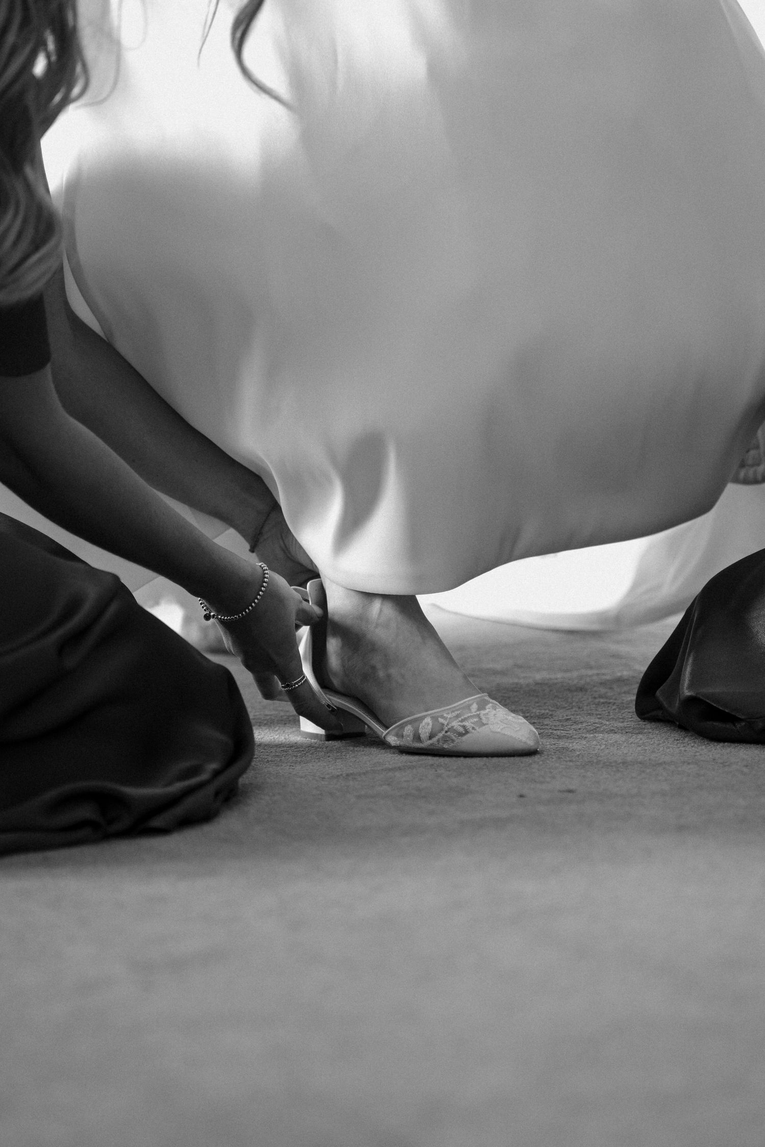 Black and white detail shot of wedding dress hem and shoes on concrete floor.