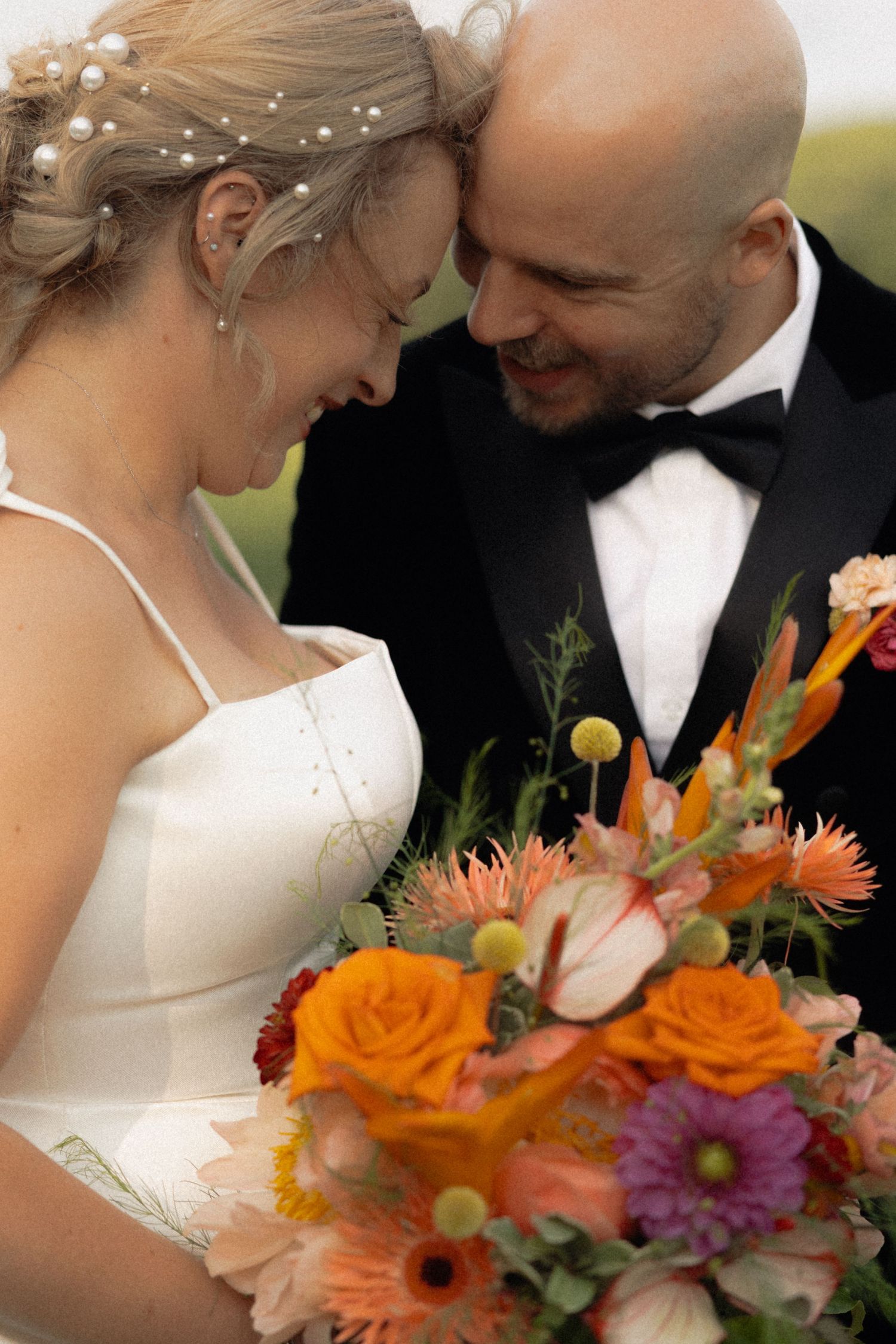 Romantic wedding couple embracing with vibrant orange and purple floral bouquet in golden sunlight.