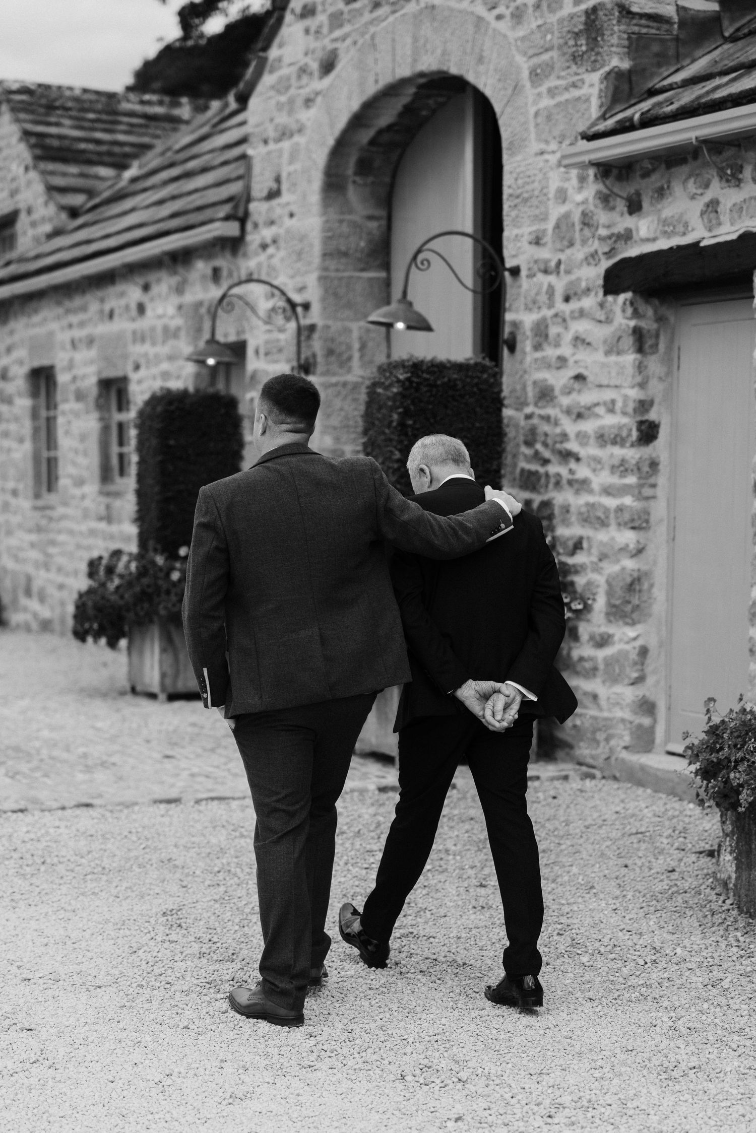 Two people walking arm in arm towards stone building entrance.