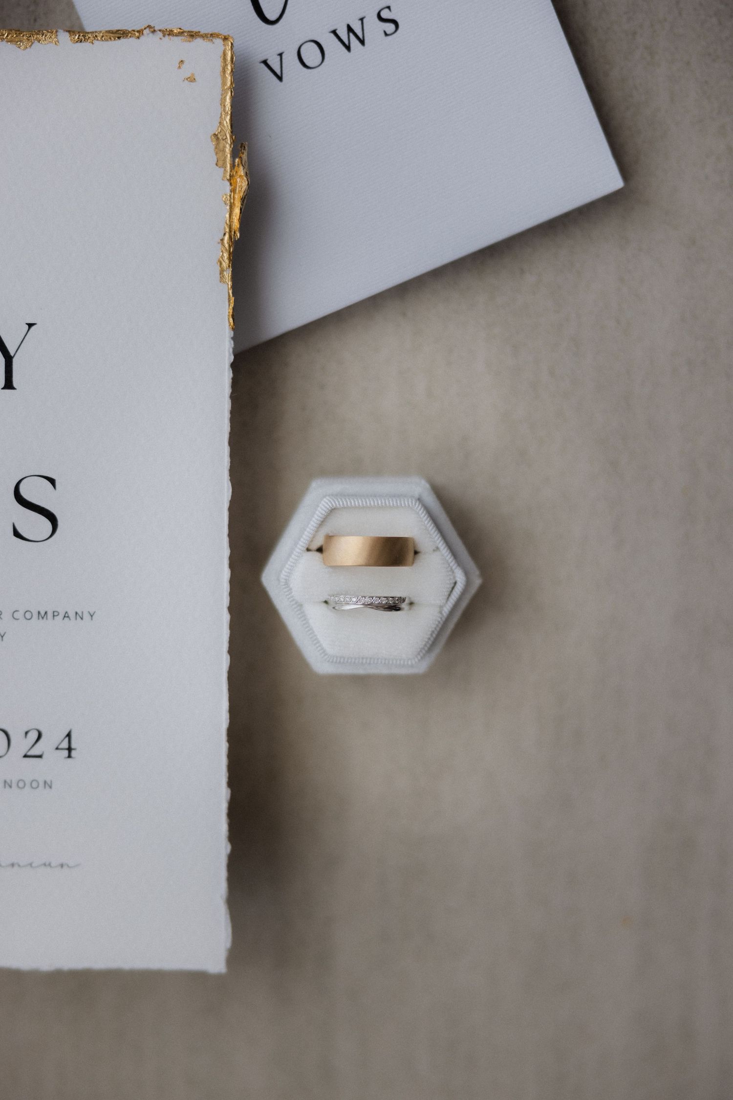 Close-up of wedding stationery details showing hexagonal ring box and torn paper edges.