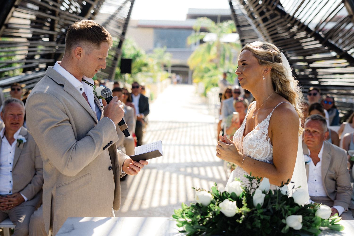 Wedding ceremony under pergola with guests watching emotional exchange.