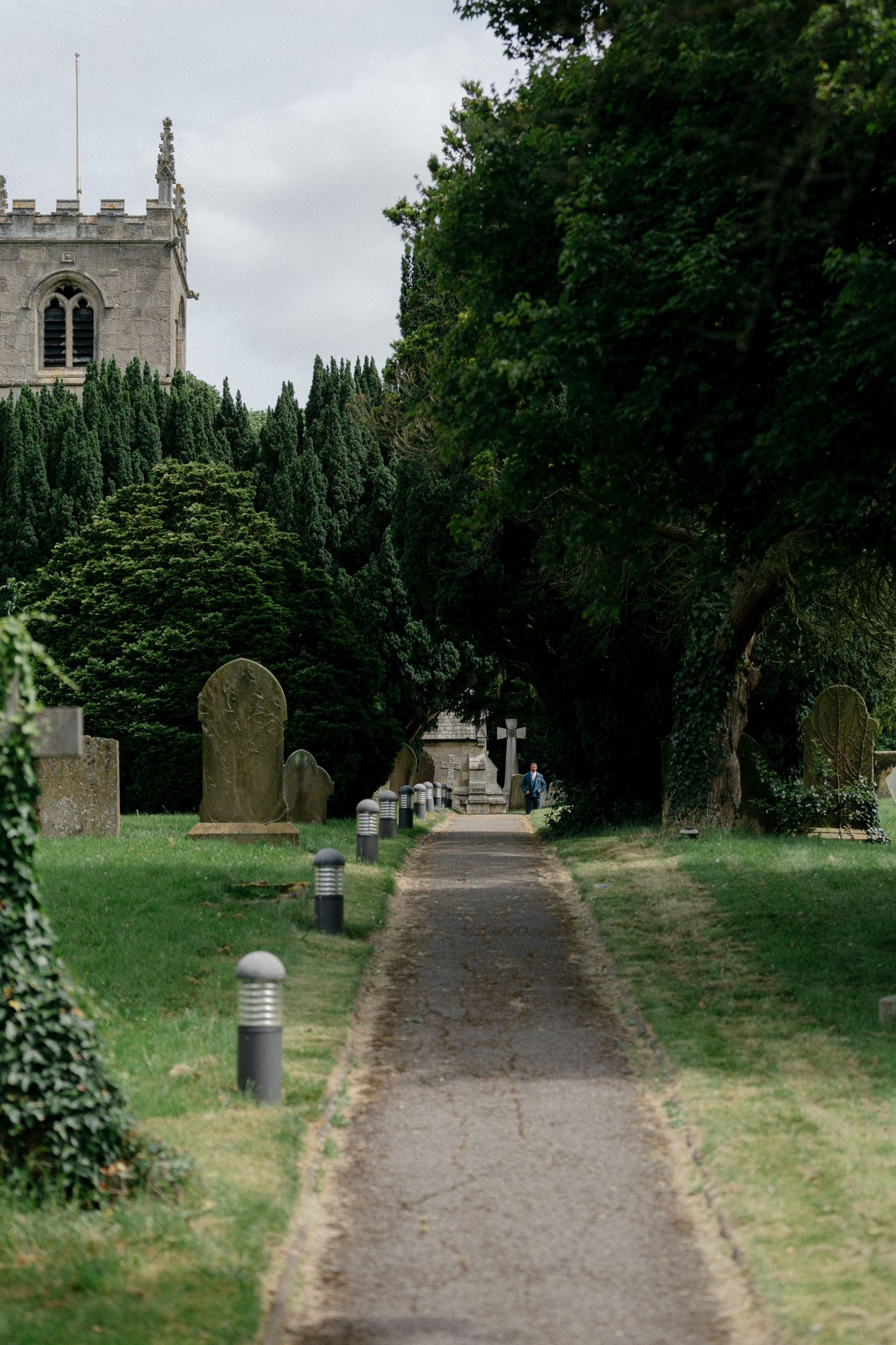 A stone church pathway lined with trees leads to a historic chapel tower.