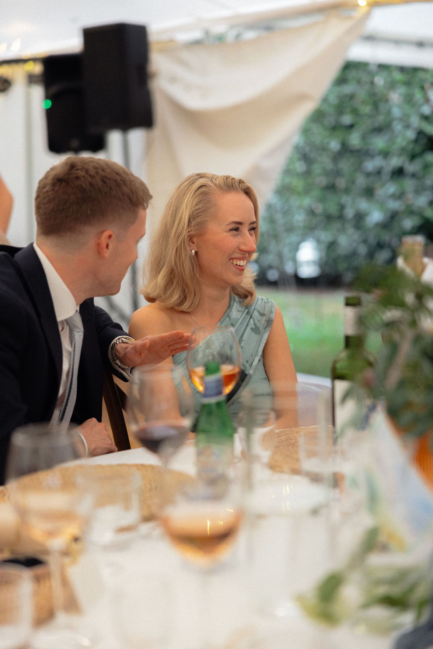 Guests share laughs during wedding reception dinner under tent lighting.