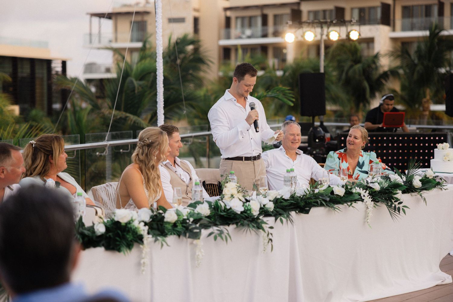 Wedding reception dinner table decorated with elegant white floral arrangements and string lights overhead.