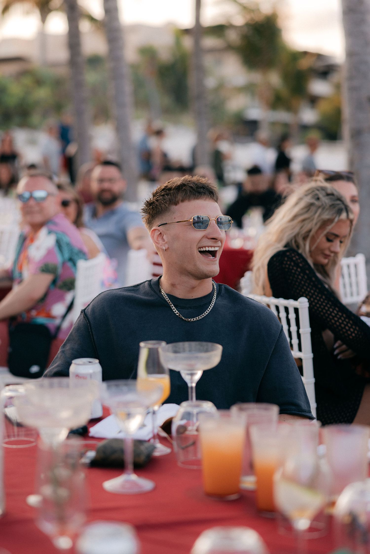 A group of guests laughing and enjoying drinks at an outdoor reception with red tablecloths.