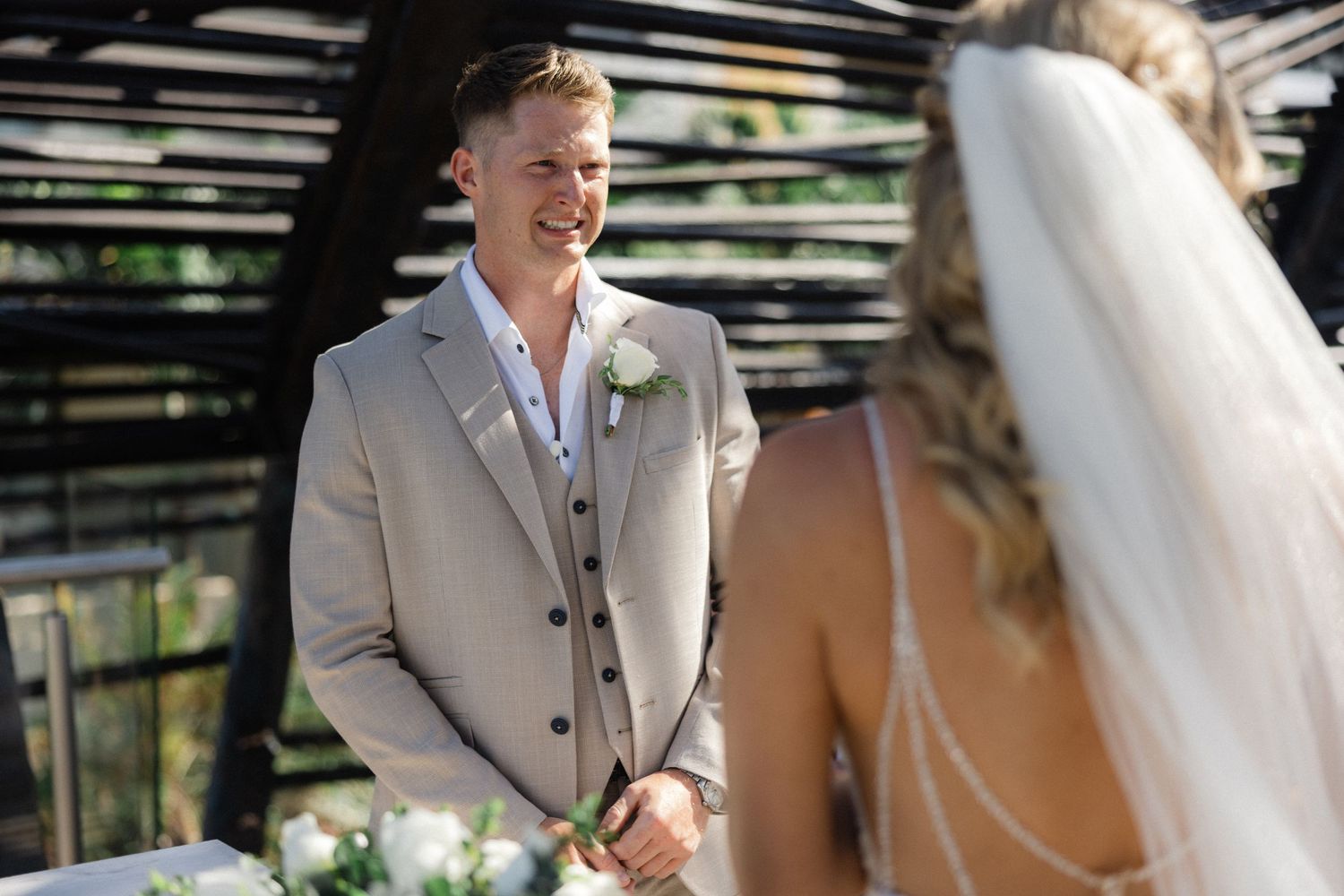 Outdoor wedding celebration with guests seated under modern architectural structure.