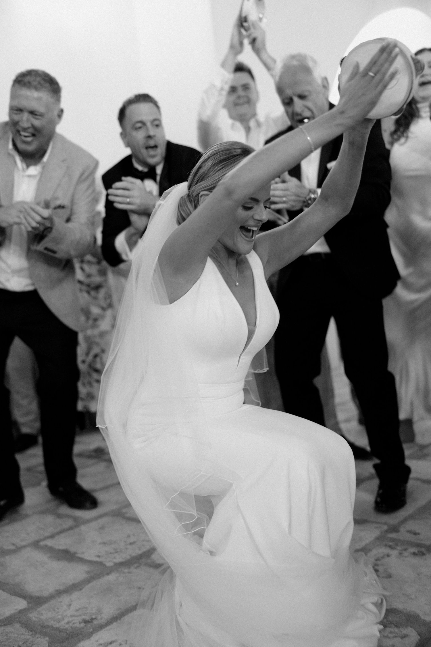 A joyful wedding celebration with guests dancing in formal attire.