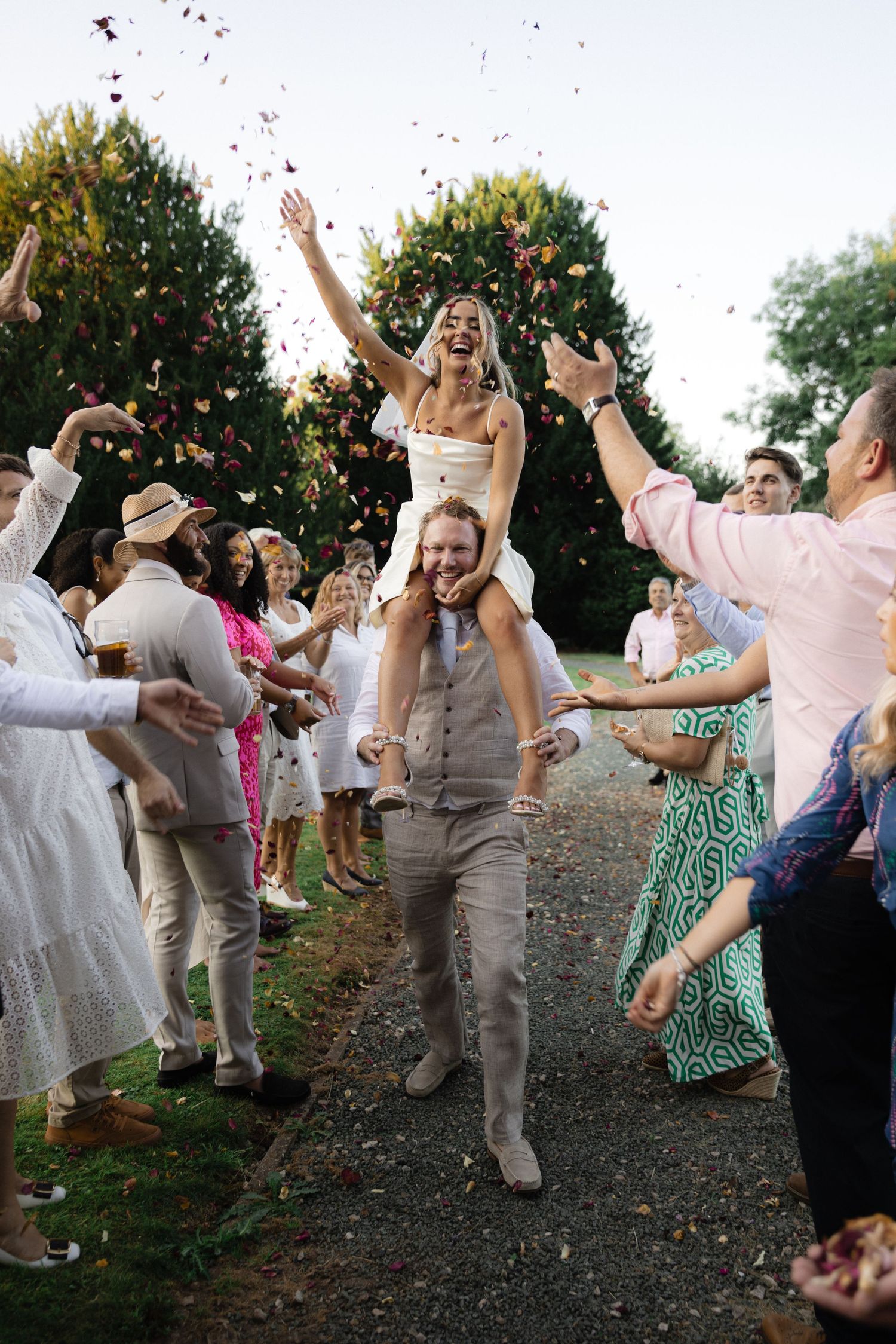 Wedding guests throwing confetti during an outdoor celebration with people jumping and cheering.