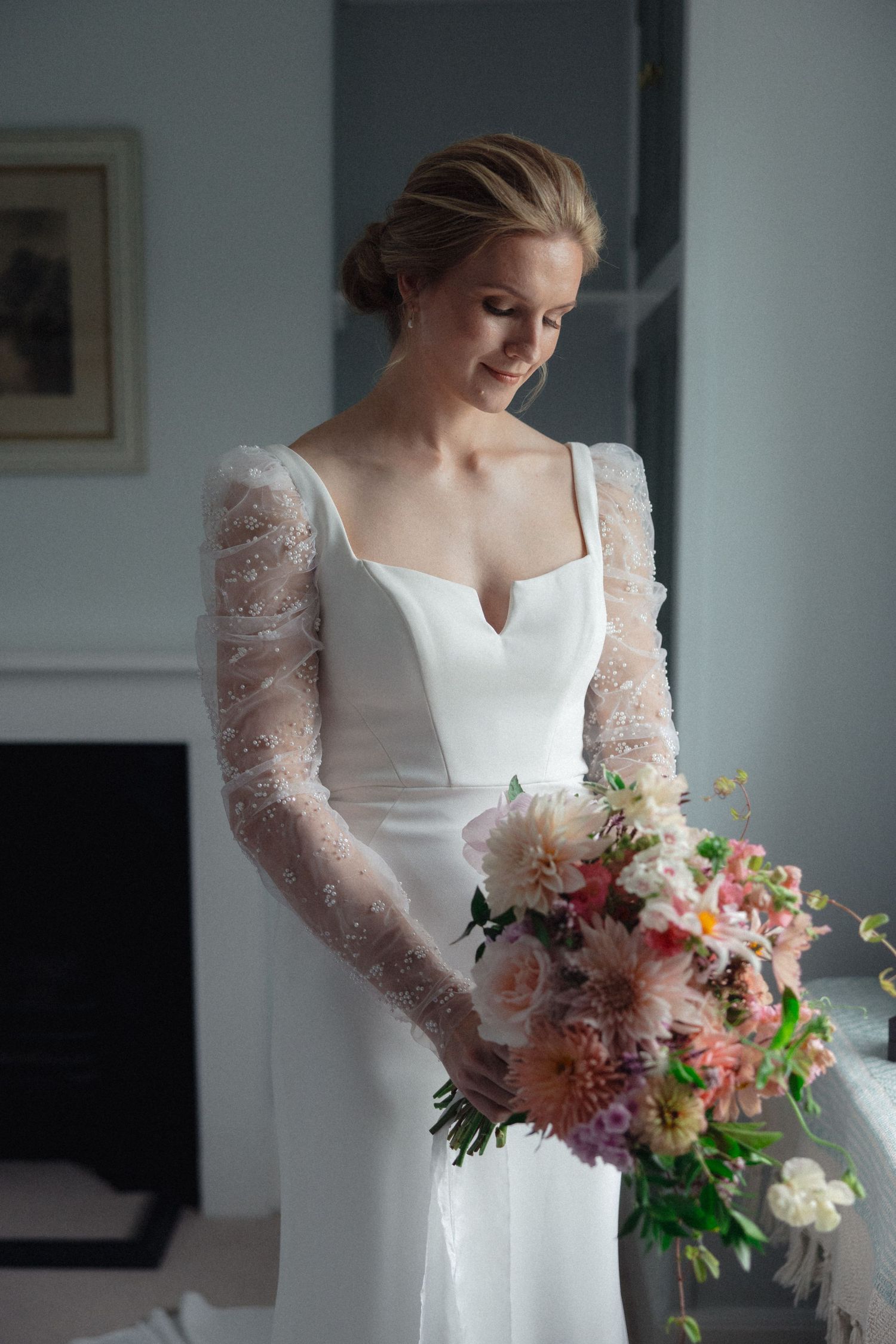 Bride in white lace-sleeved dress holding colorful spring wedding bouquet.