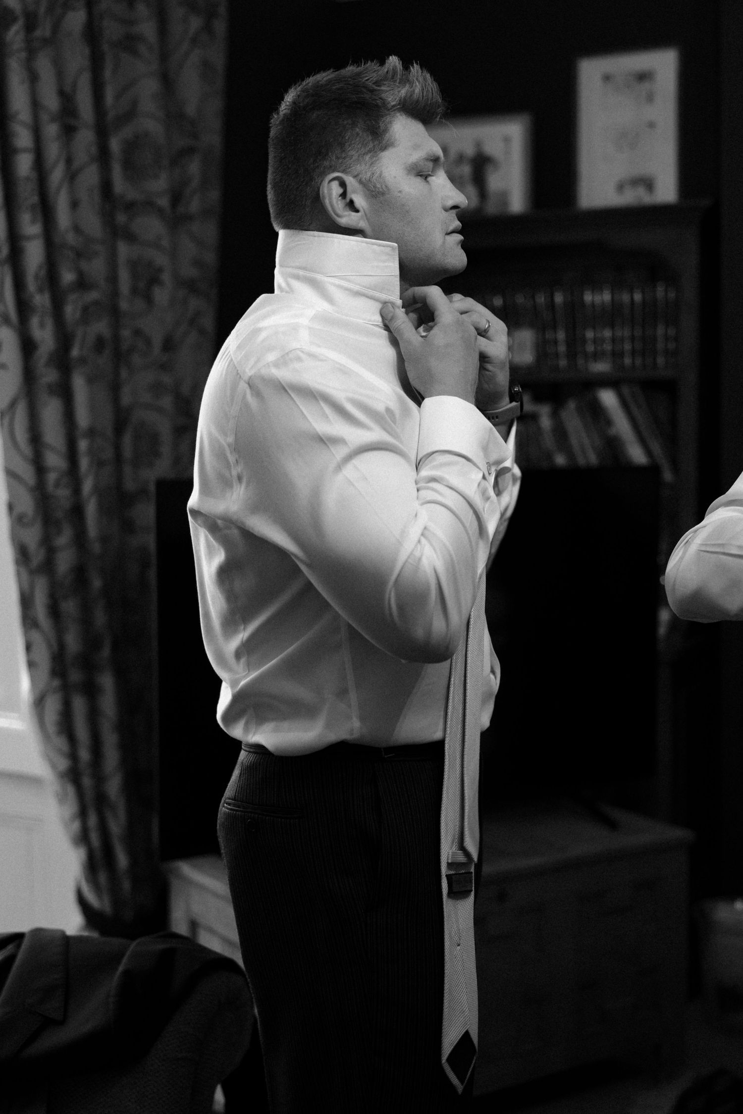 Man in white shirt adjusts tie while getting ready.