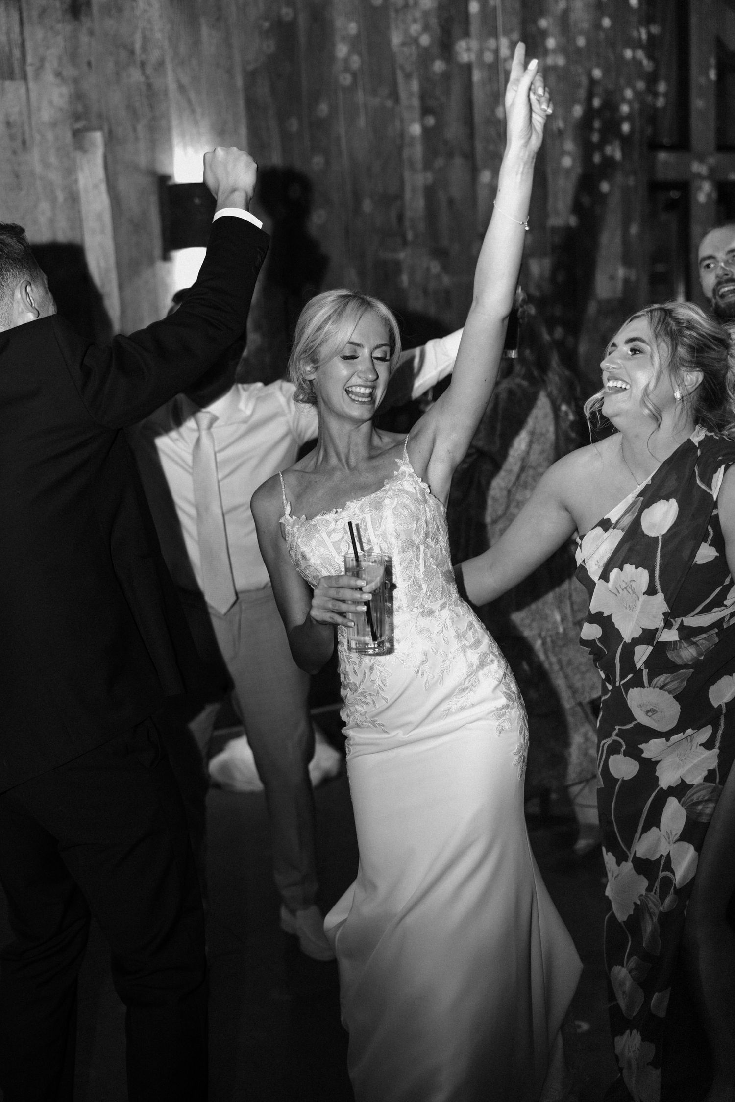 Wedding guests dancing and celebrating with raised arms in a dimly lit venue.