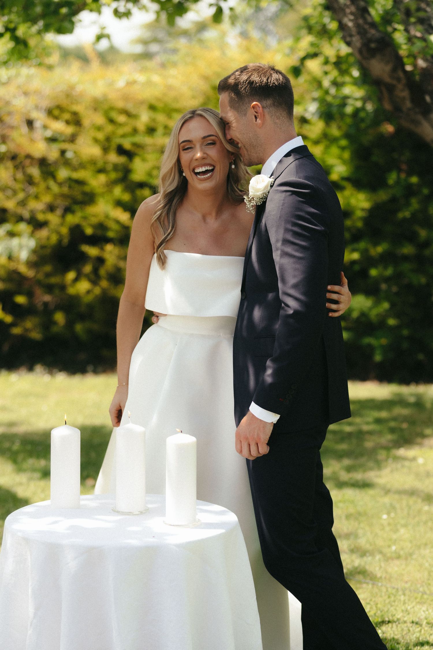 A joyful moment shared between a couple next to a table with white candles during their outdoor wedding.