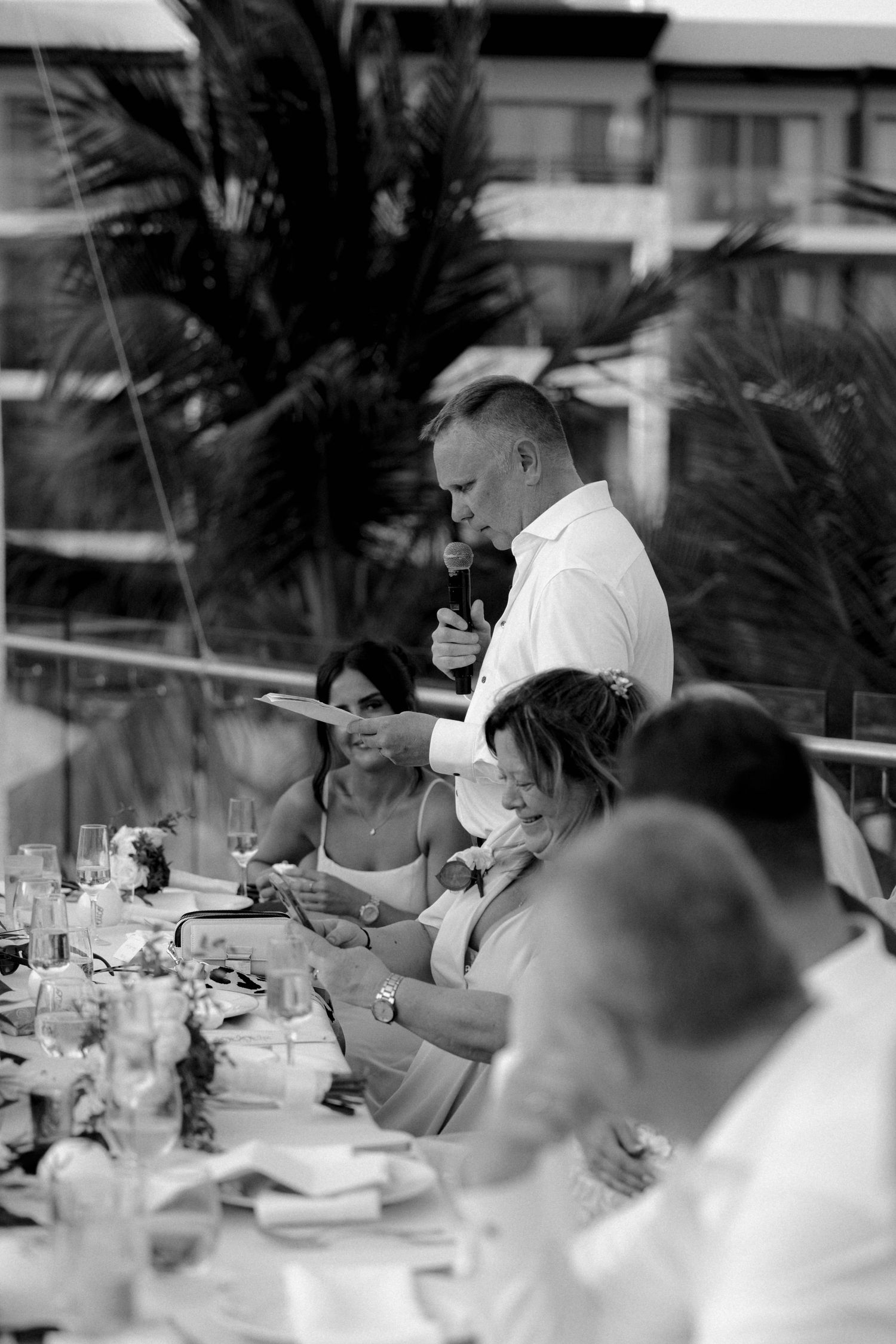 Black and white photo of wedding reception guests raising glasses in toast.