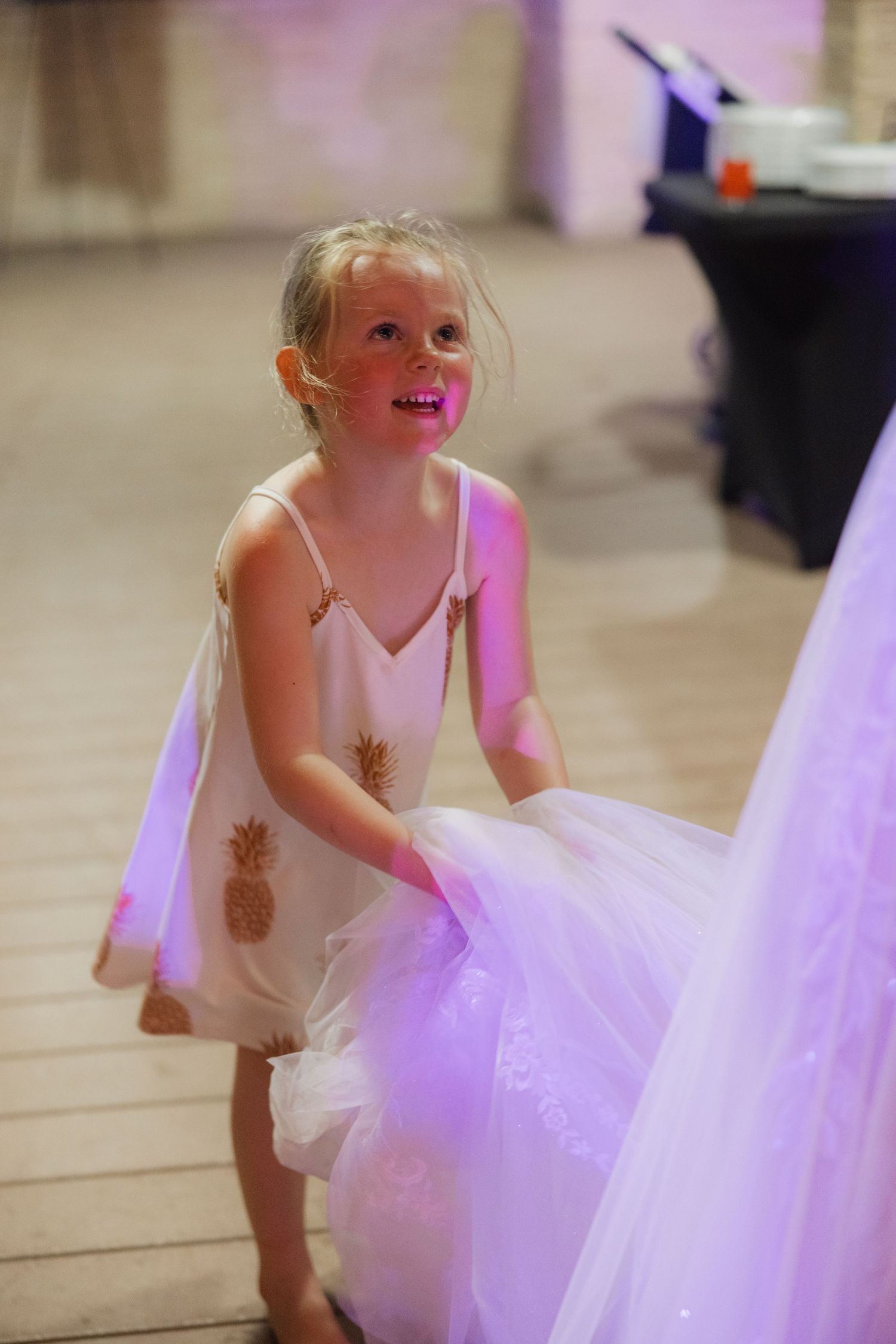 Young flower girl in a white dress with pineapple pattern twirls on the dance floor.
