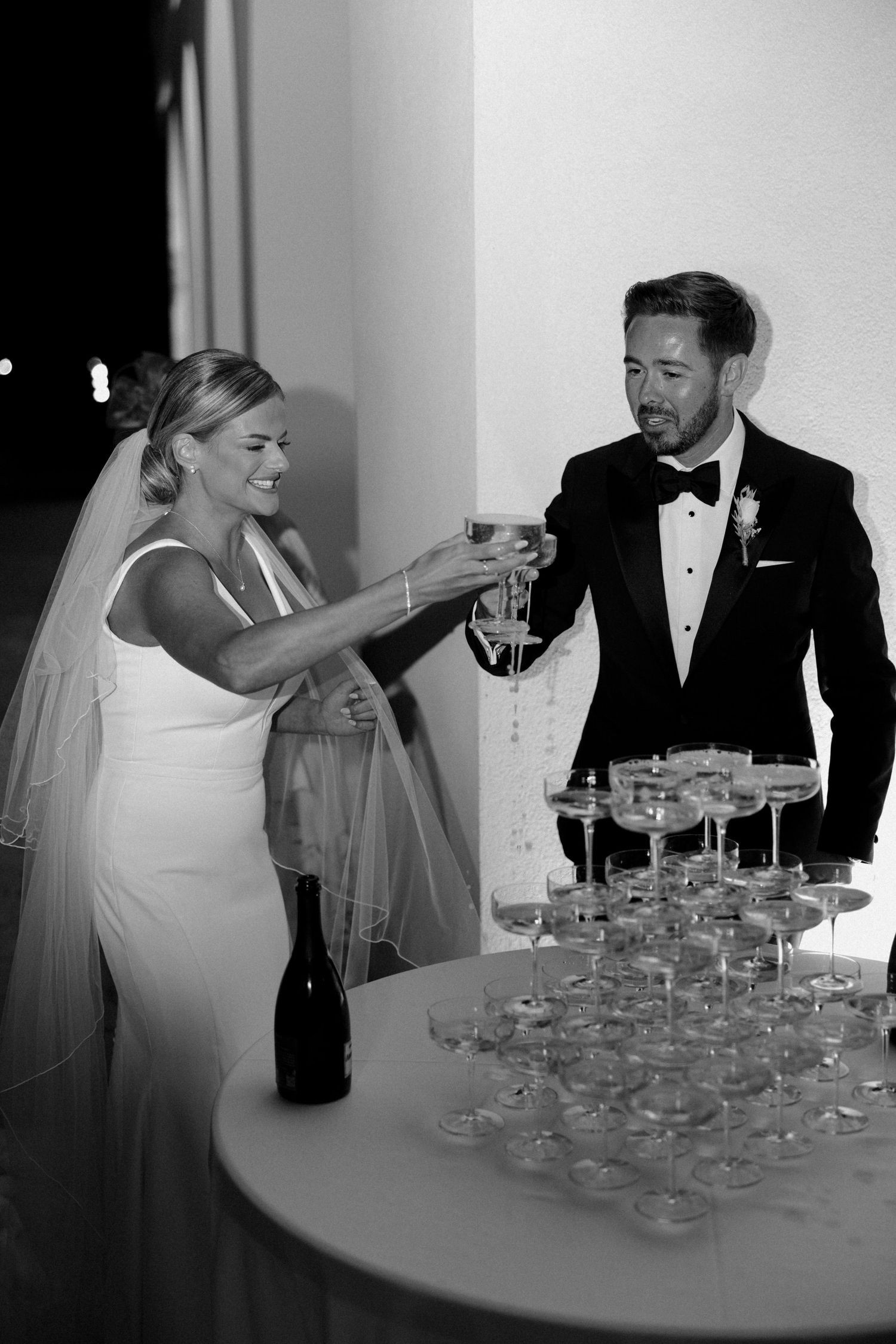 Elegant couple in formal attire pouring drinks into a champagne tower.