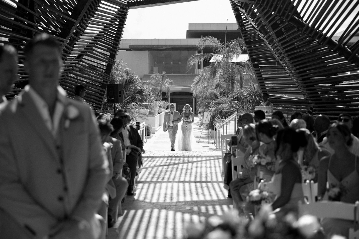 Black and white image of people walking through a modern architectural space with dramatic shadows.