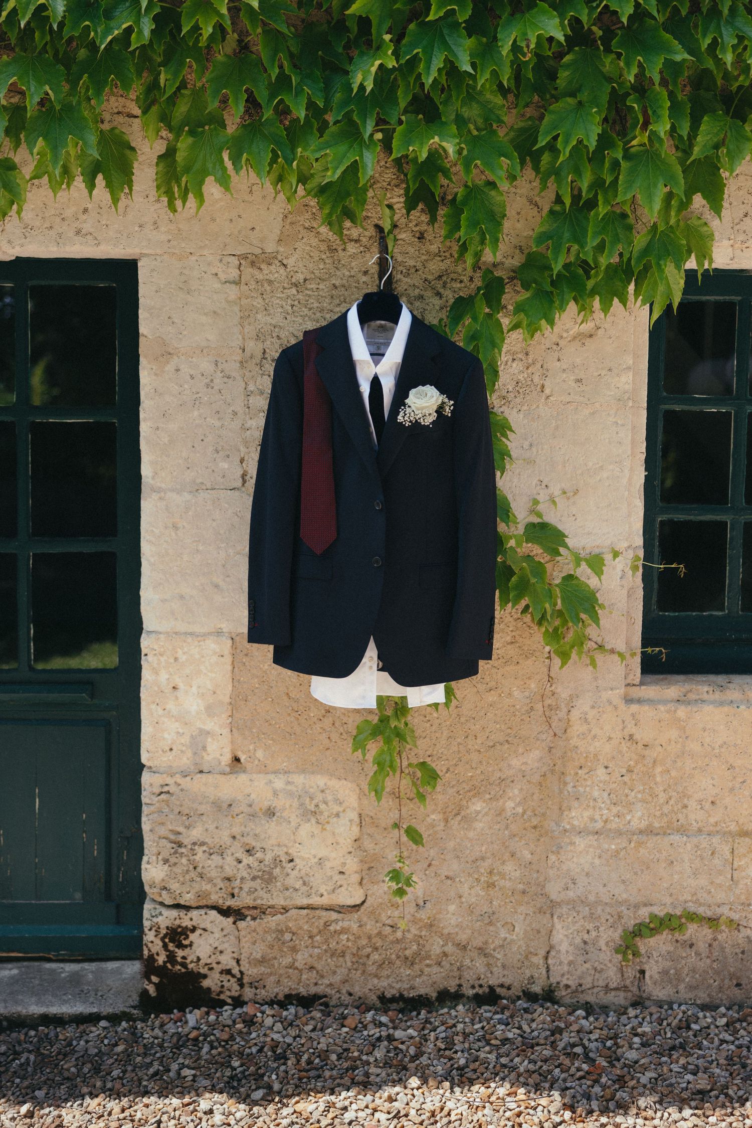 Black suit jacket hanging against stone wall with green ivy leaves.