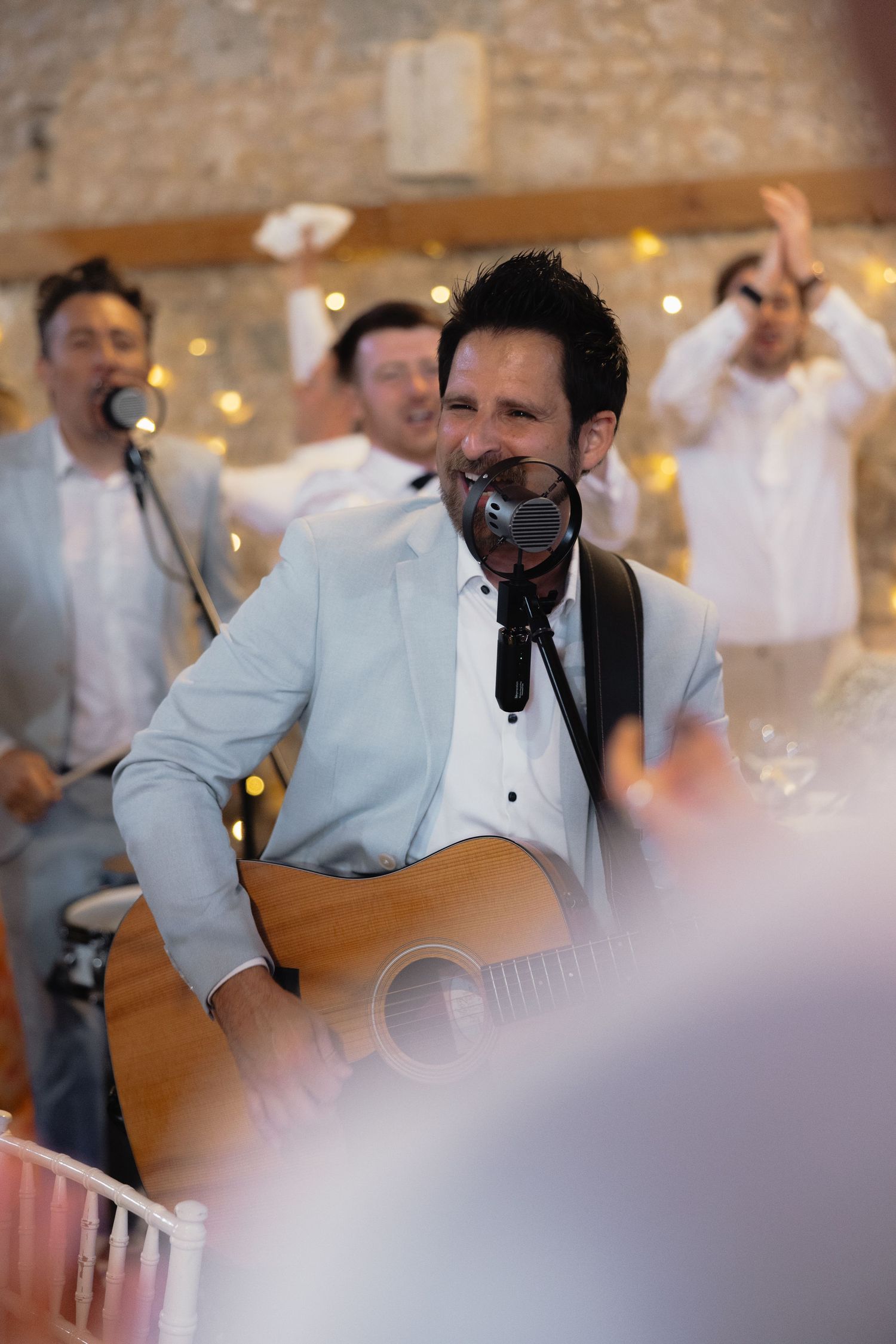 Musician in light blue jacket plays acoustic guitar at wedding reception.