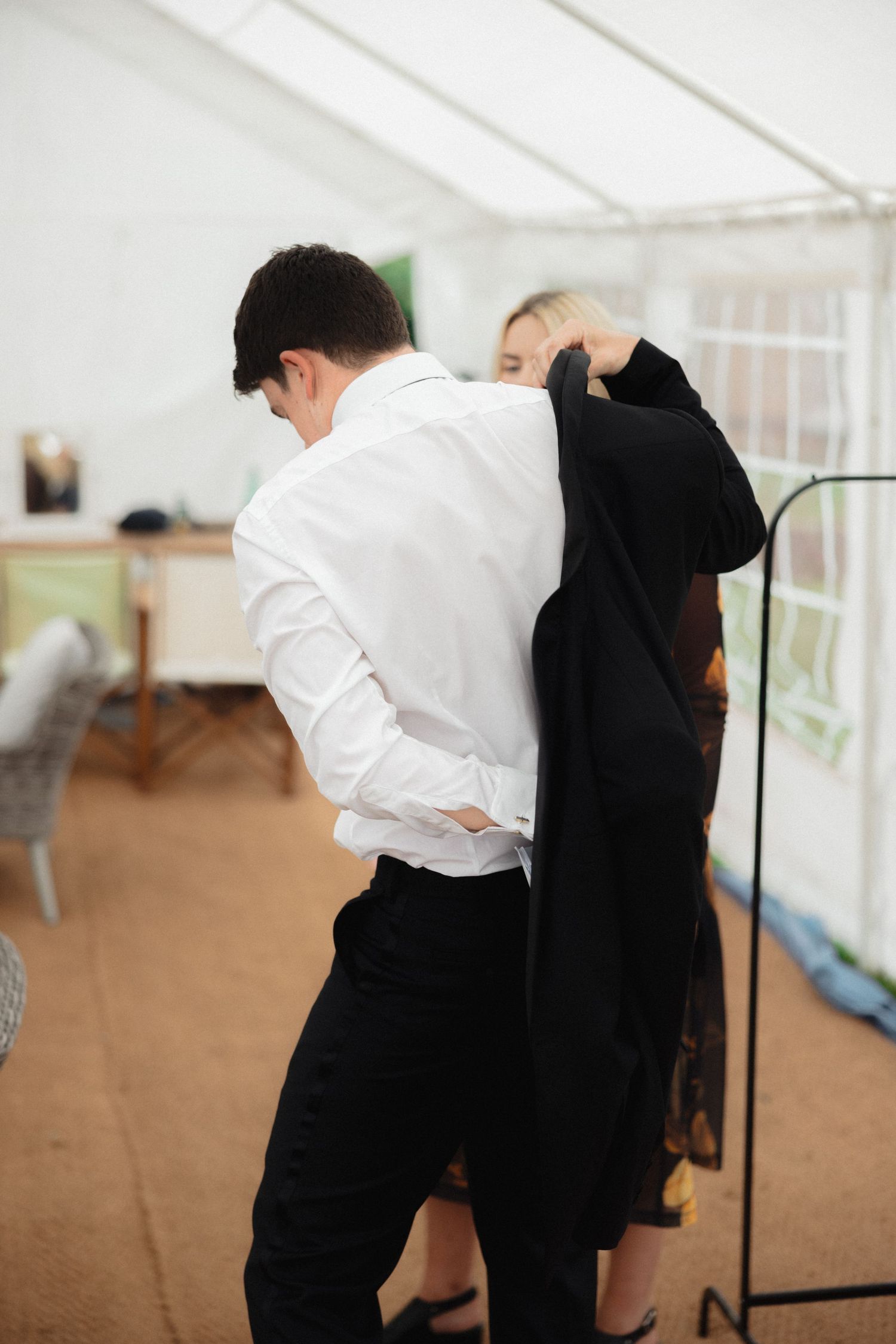 Wedding preparation scene showing black and white formal attire being adjusted in a bright room.