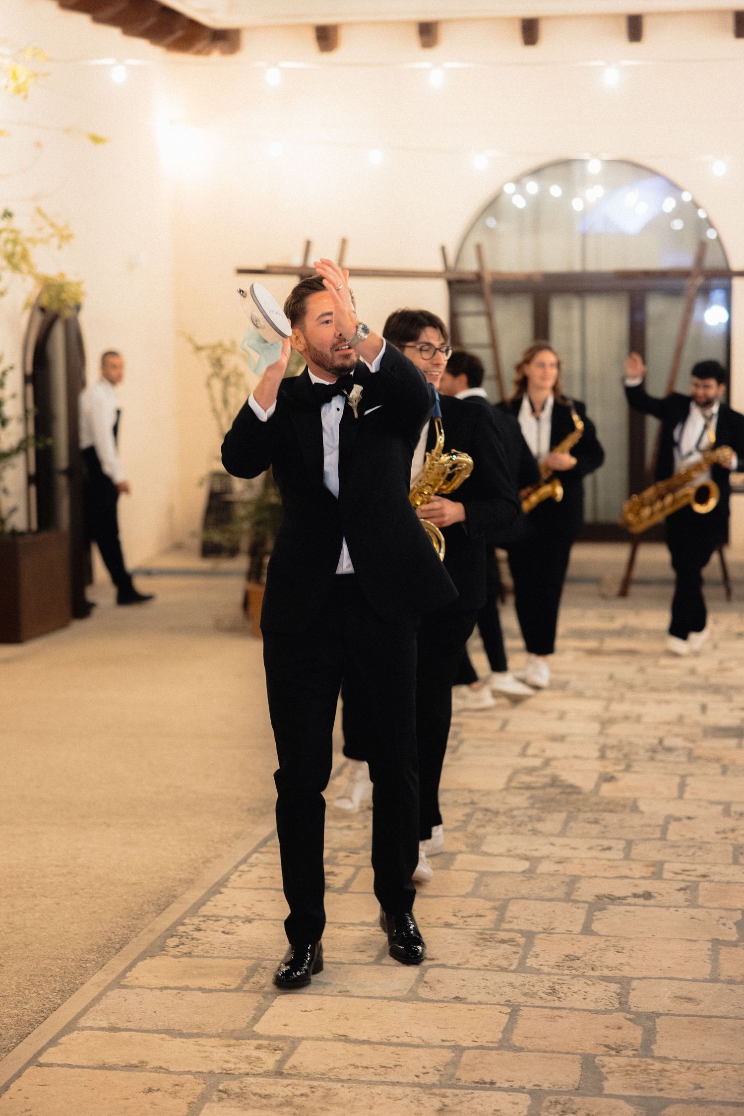 Musicians in formal black attire performing while walking through an elegant stone hallway.