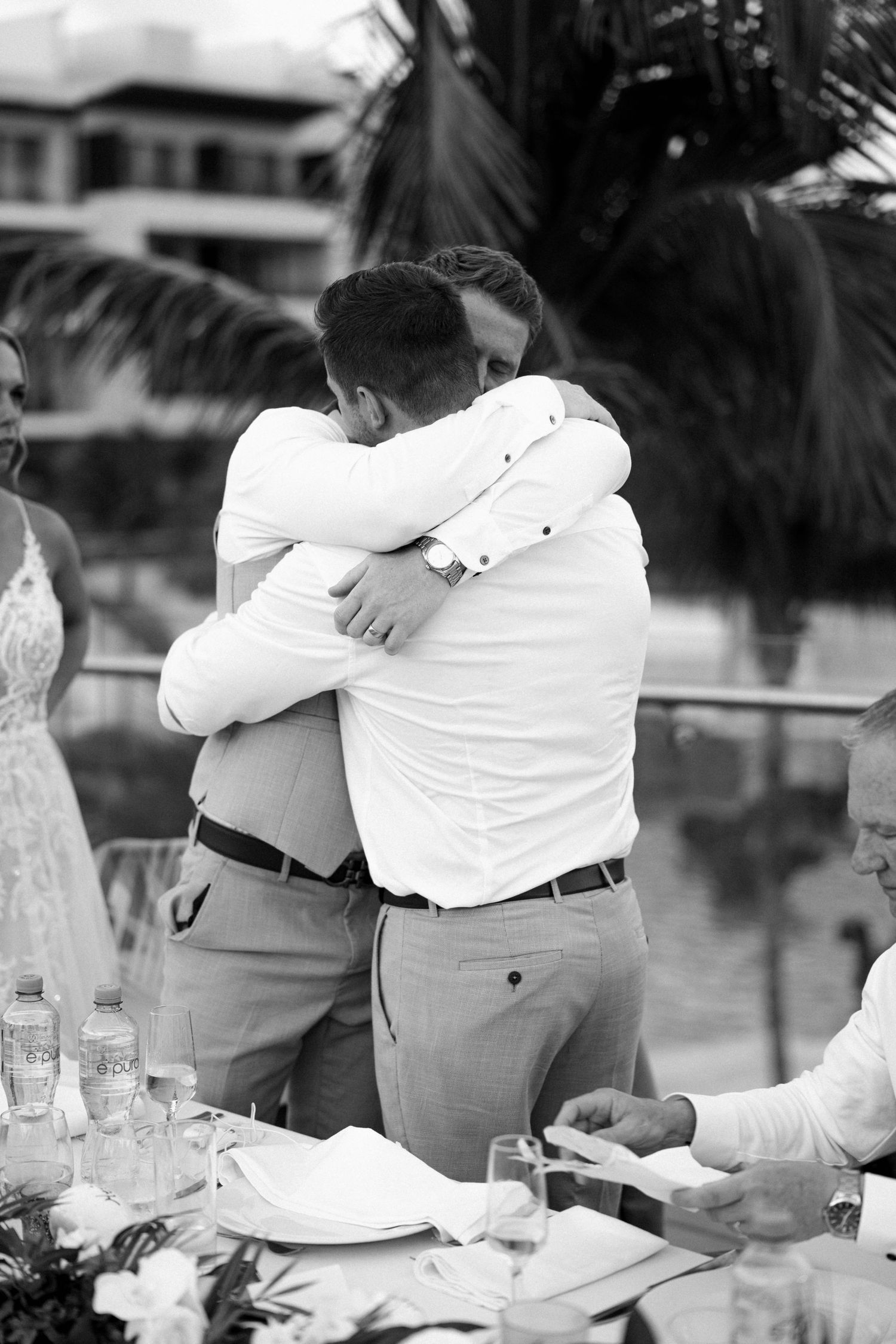 Wedding party members hugging and embracing during emotional reception moment.