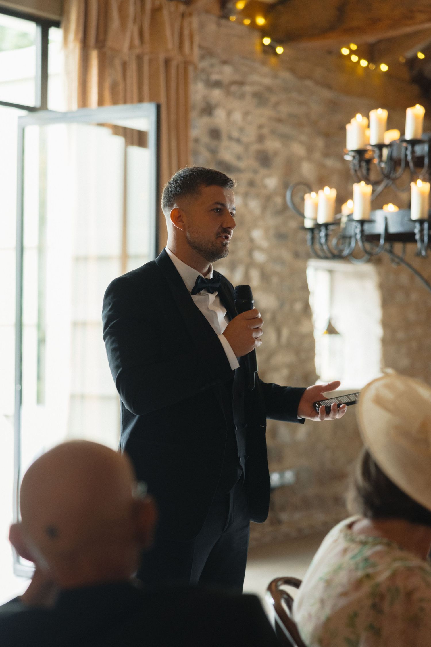 A speaker addresses guests at an elegant stone-walled venue with natural lighting.