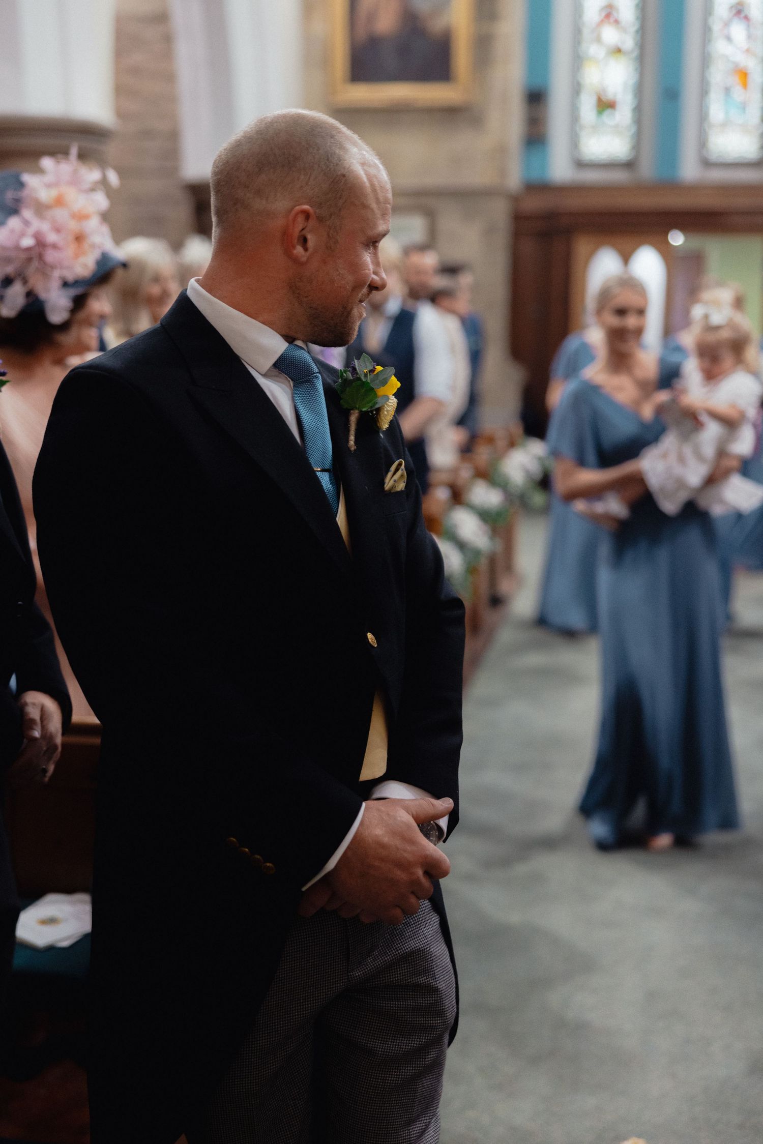 Wedding guests and attendants gathered inside a traditional church with blue walls and stained glass windows.