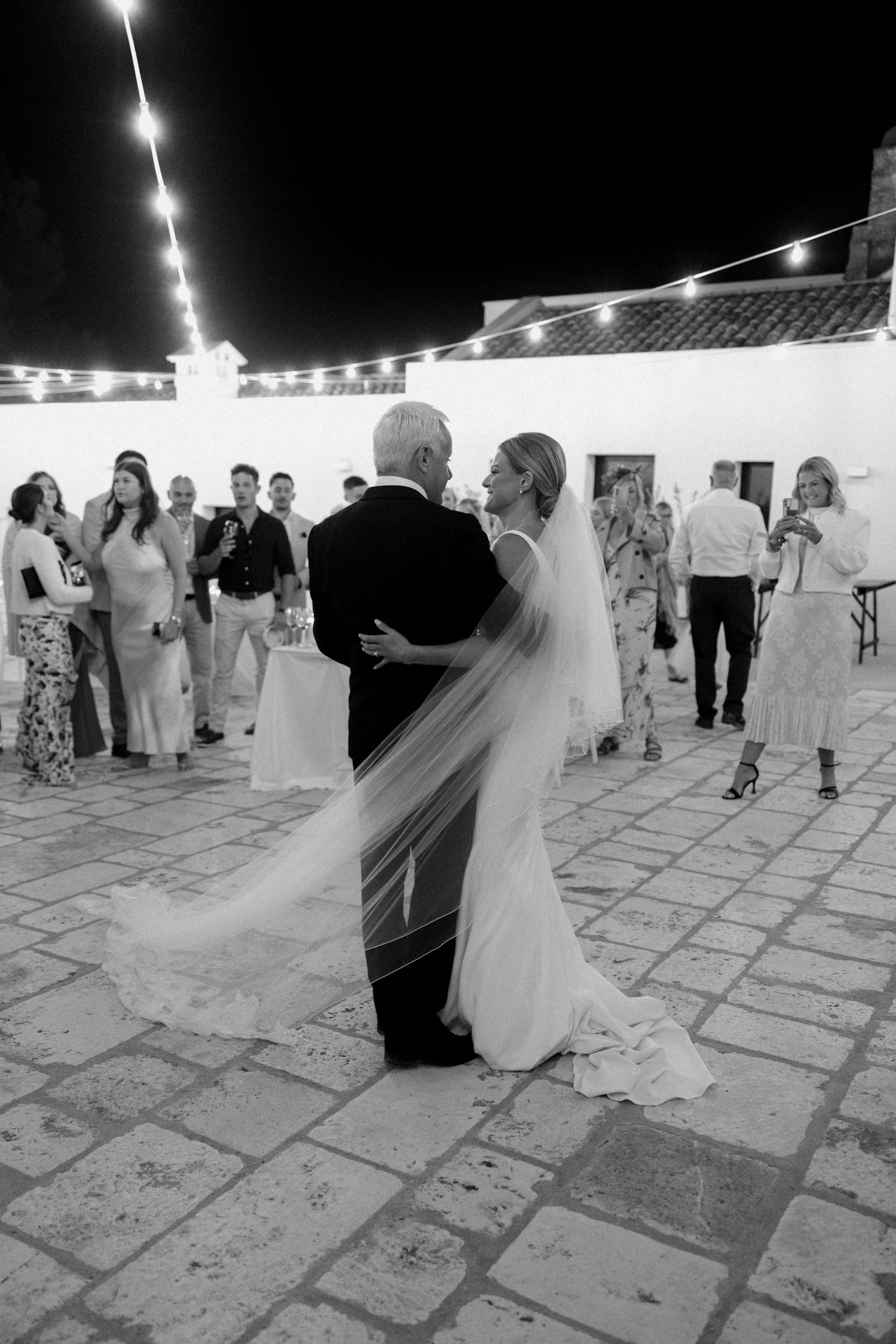Couples dancing on a stone patio under string lights at night.