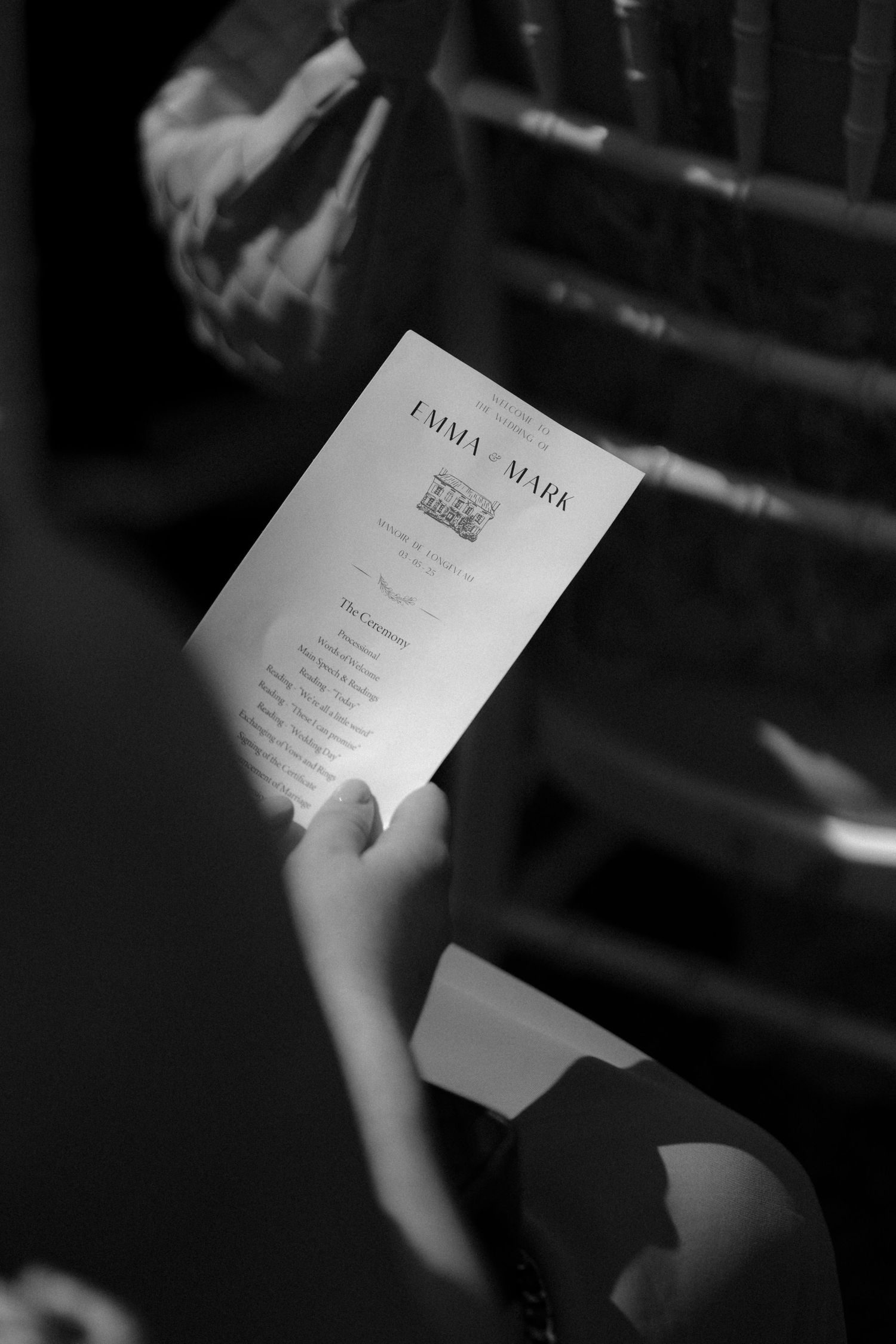 A black and white photo of a wedding program being held by a guest.