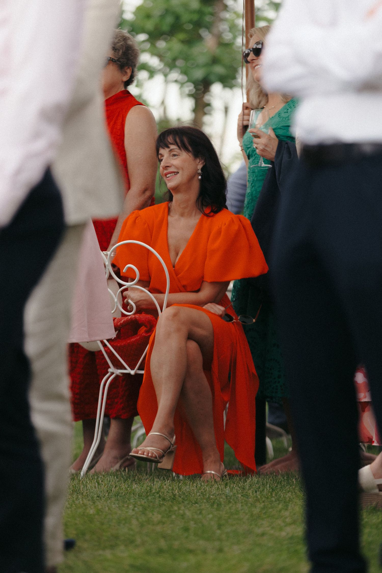 Wedding guests in bright red dresses seated on white chairs during outdoor ceremony.