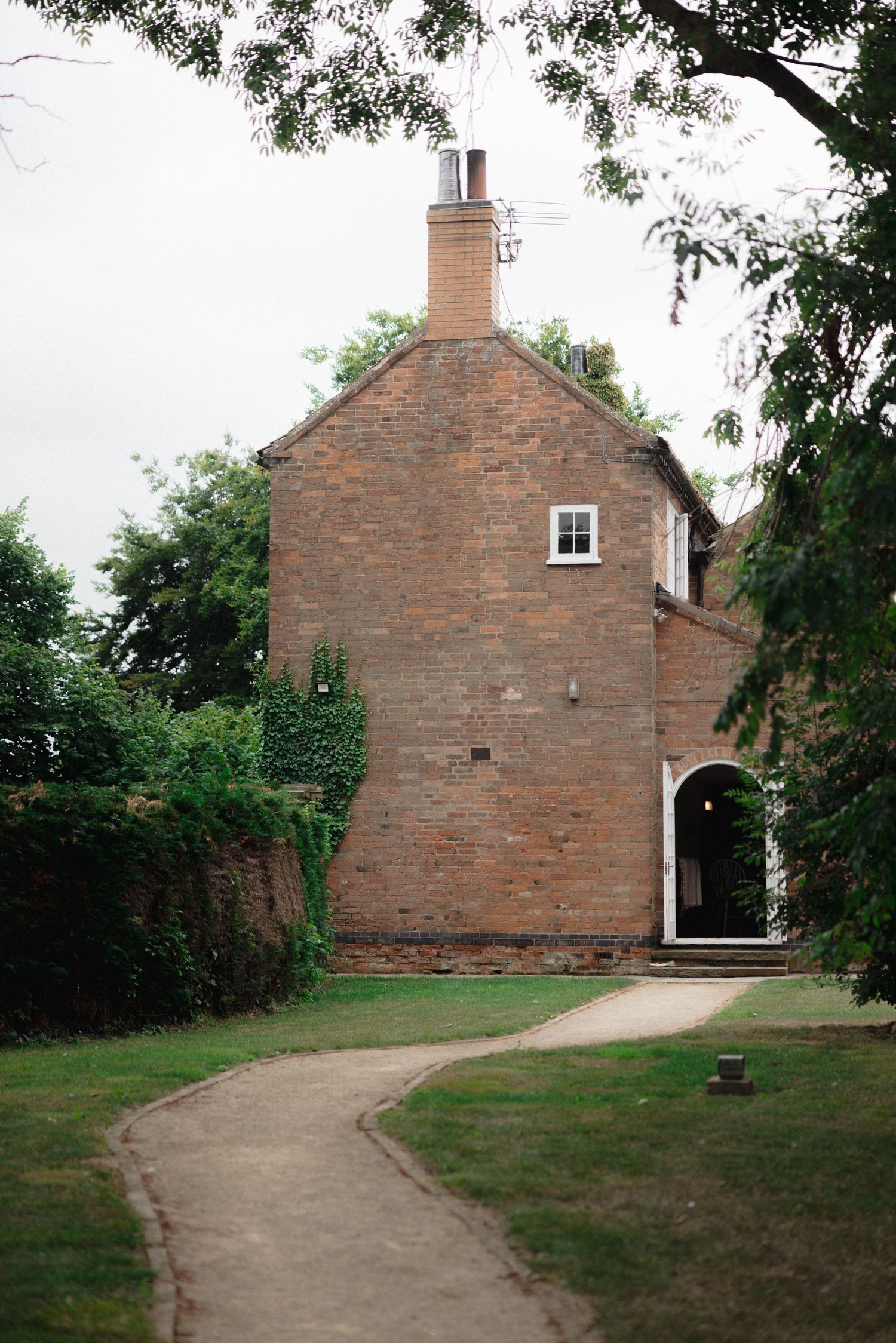 Historic brick building with arched doorway and winding path through green grounds.