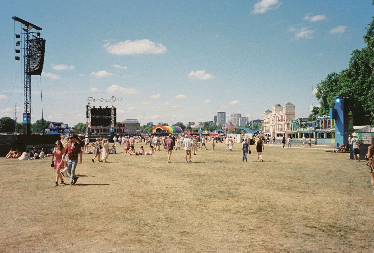 Wide sandy beach with scattered people and festival equipment under blue sky.