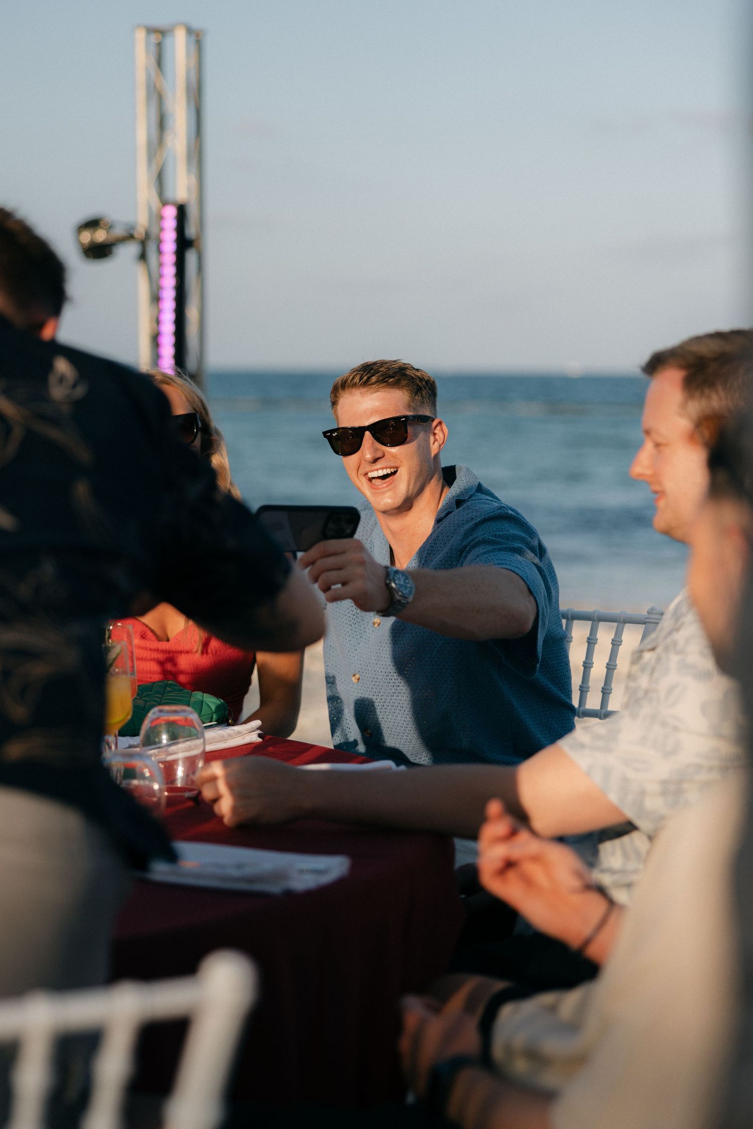 Guest smiling at outdoor beach party while seated at table.