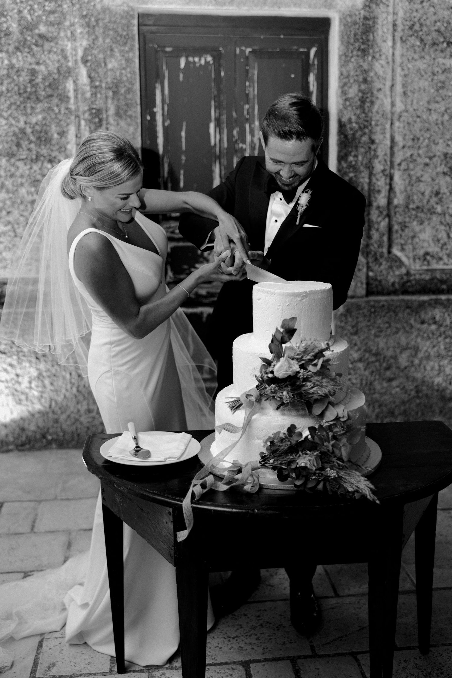 Wedding couple shares intimate moment while cutting their cake in black and white photography.