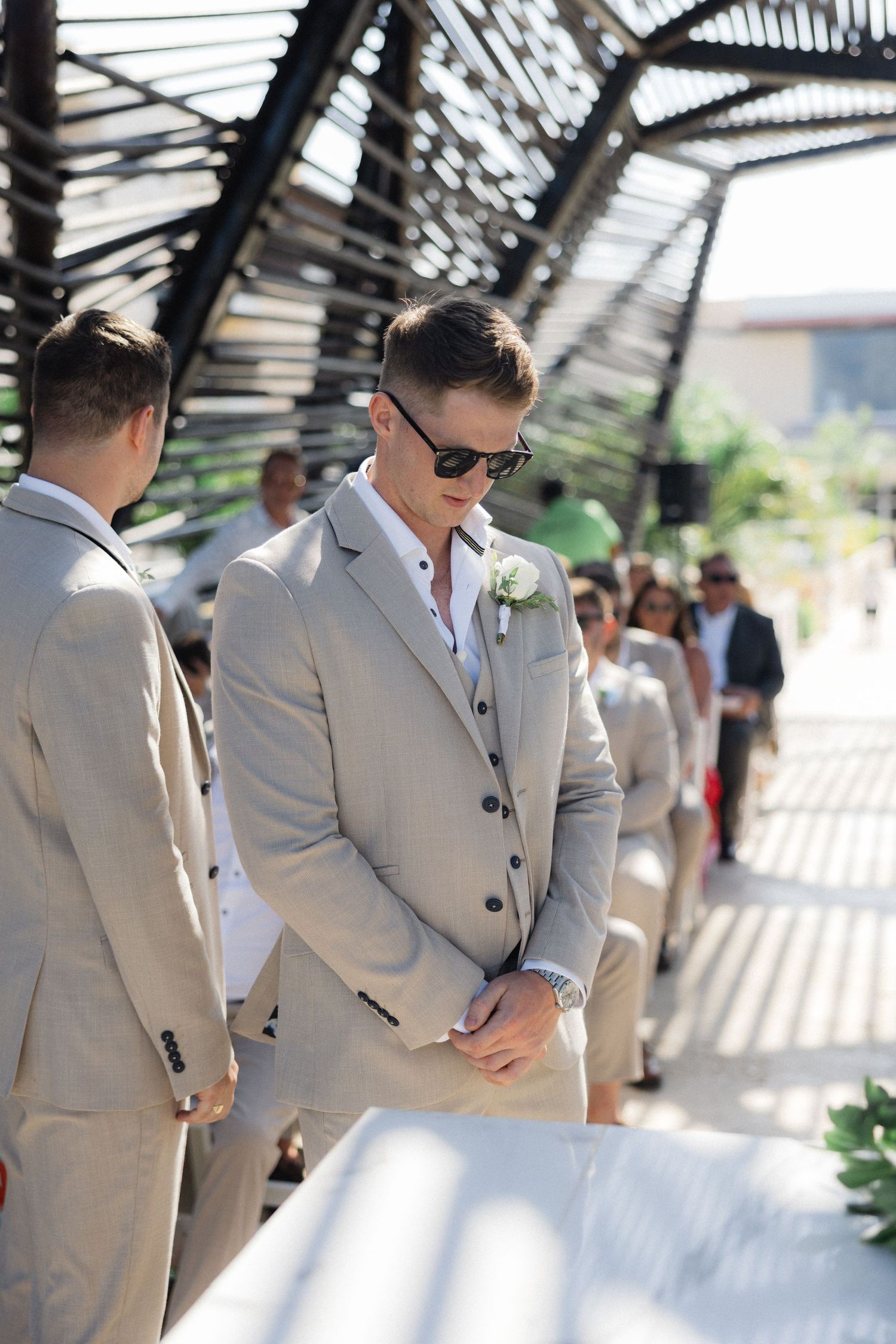 Groomsmen in light gray suits stand under modern architectural details outdoors.