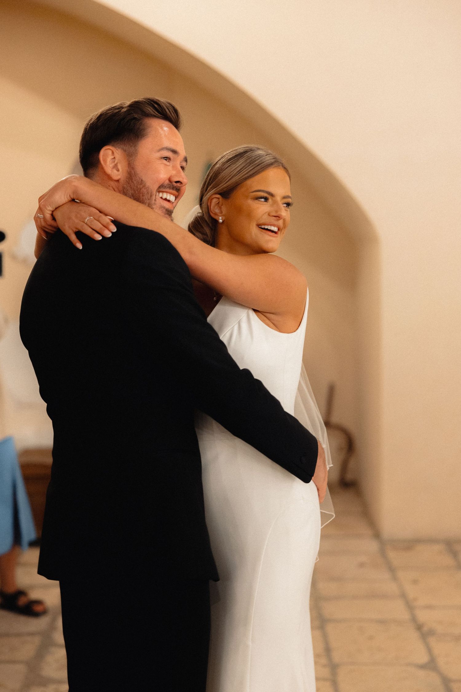 Couple sharing a joyful embrace against an arched wall.