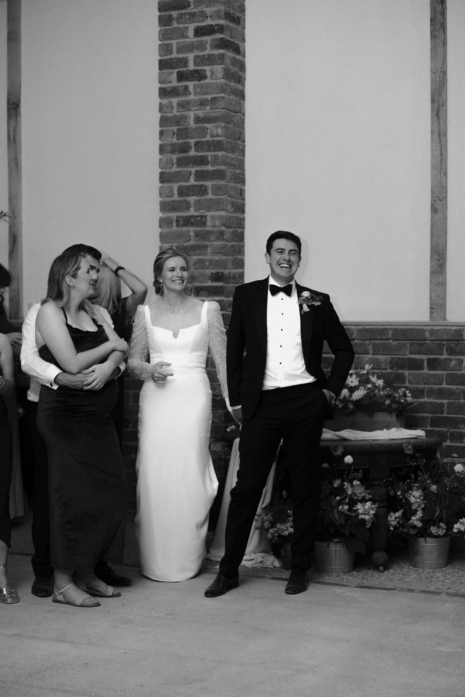 Wedding party relaxing against brick wall during reception celebrations.