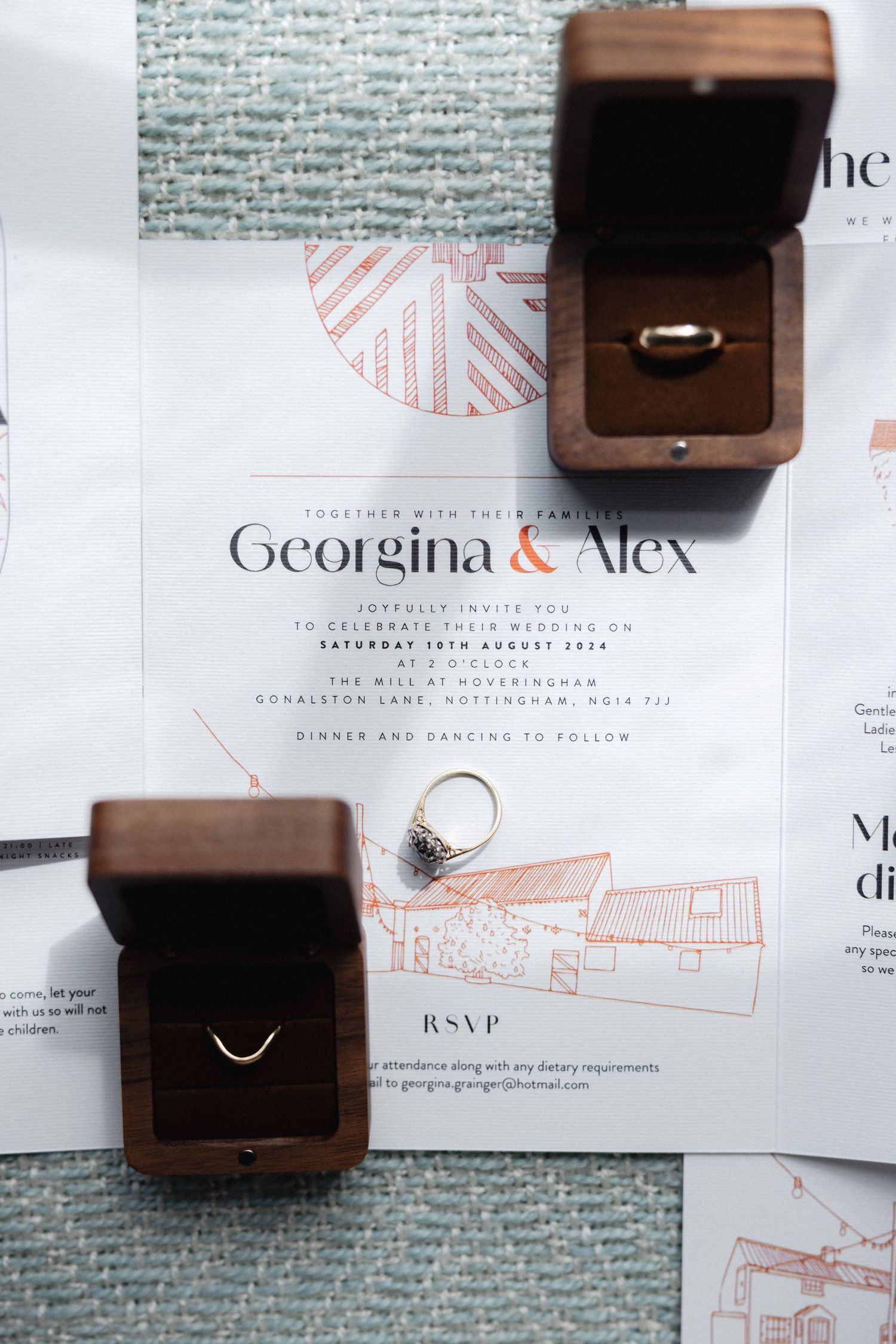 Wedding invitation suite with wooden ring boxes and geometric coral details on textured background.